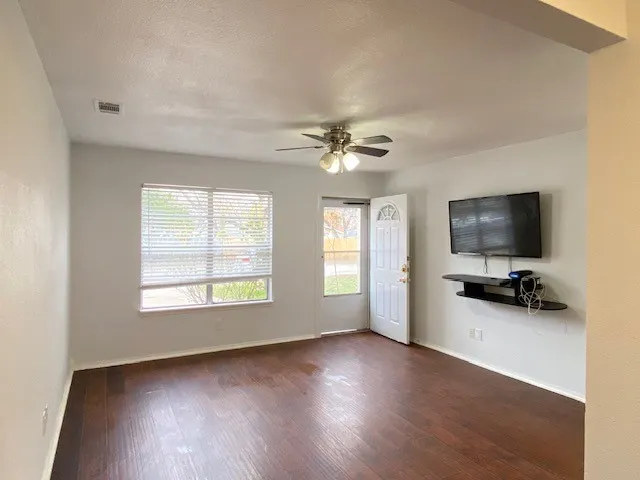 Unfurnished living room with dark wood-style floors, a ceiling fan, and a textured ceiling