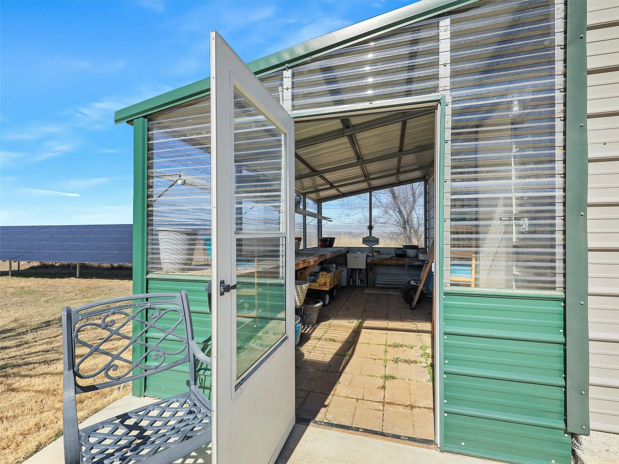 Greenhouse / single metal garage combo with concrete driveway access.