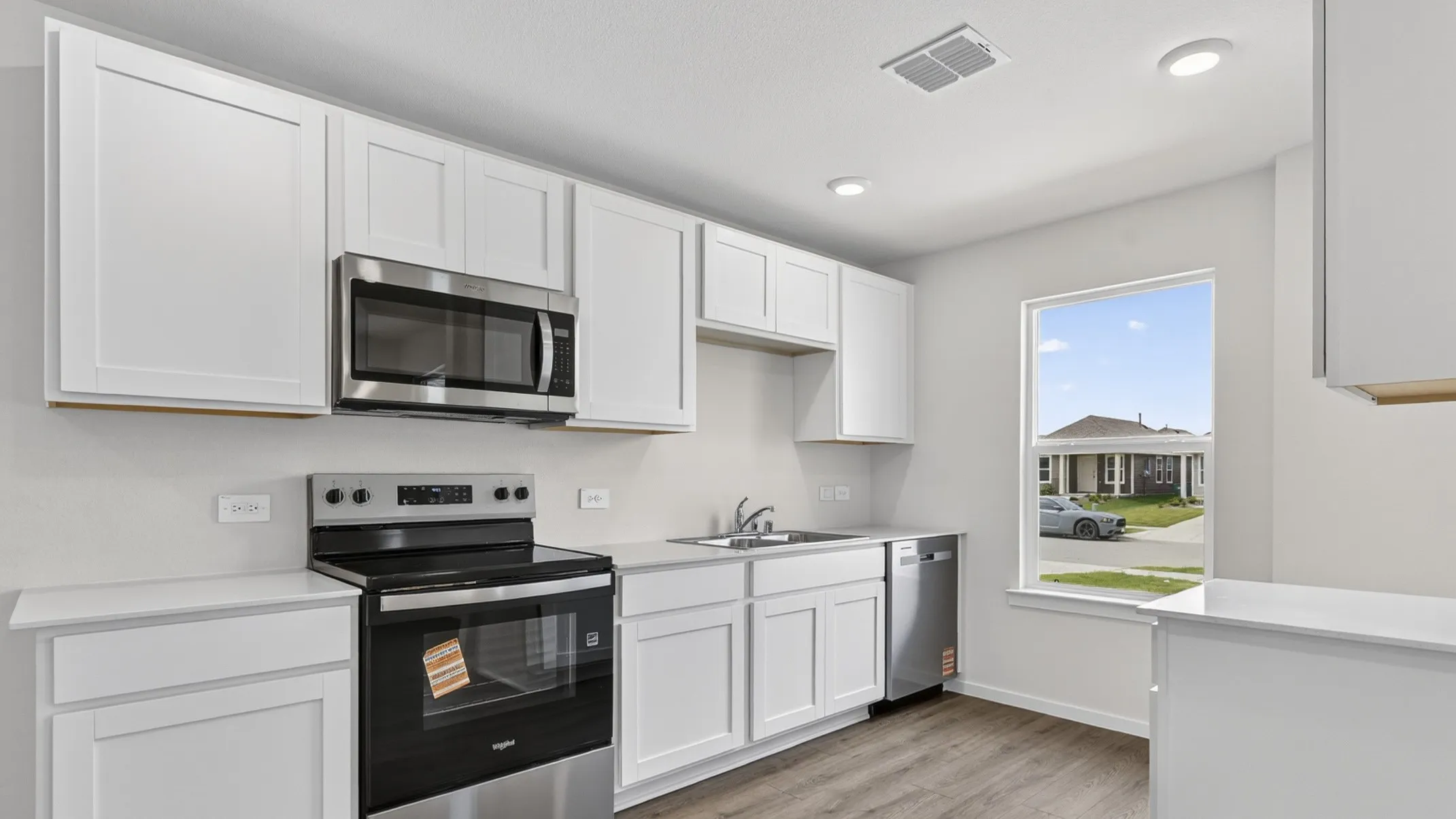 Kitchen featuring white shaker cabinetry, stainless steel appliances, light countertops, wood-finish flooring, and recessed lighting