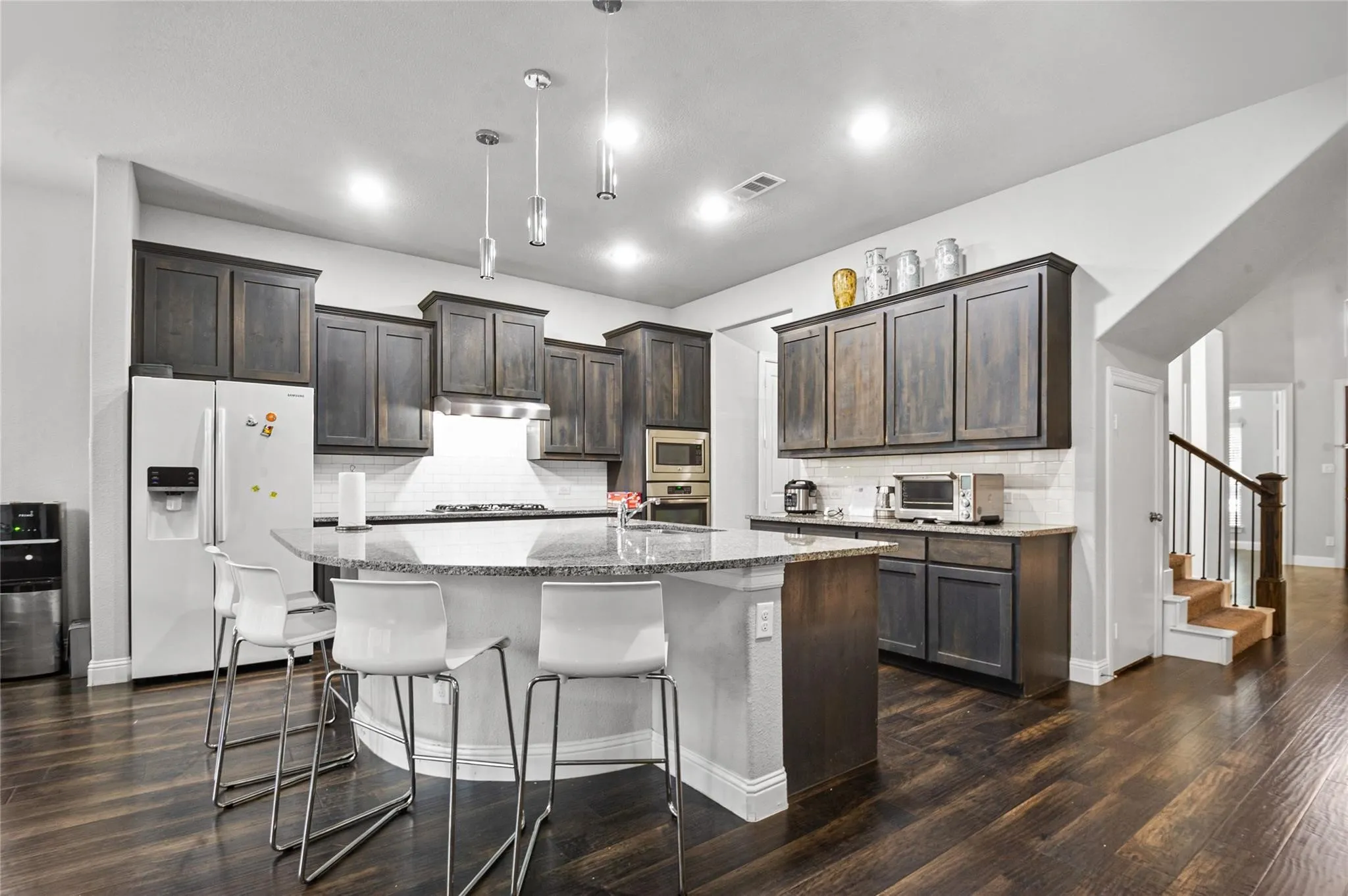 Kitchen with stainless steel appliances, dark wood finished floors, light stone countertops, a center island with sink, and dark wood finish cabinets
