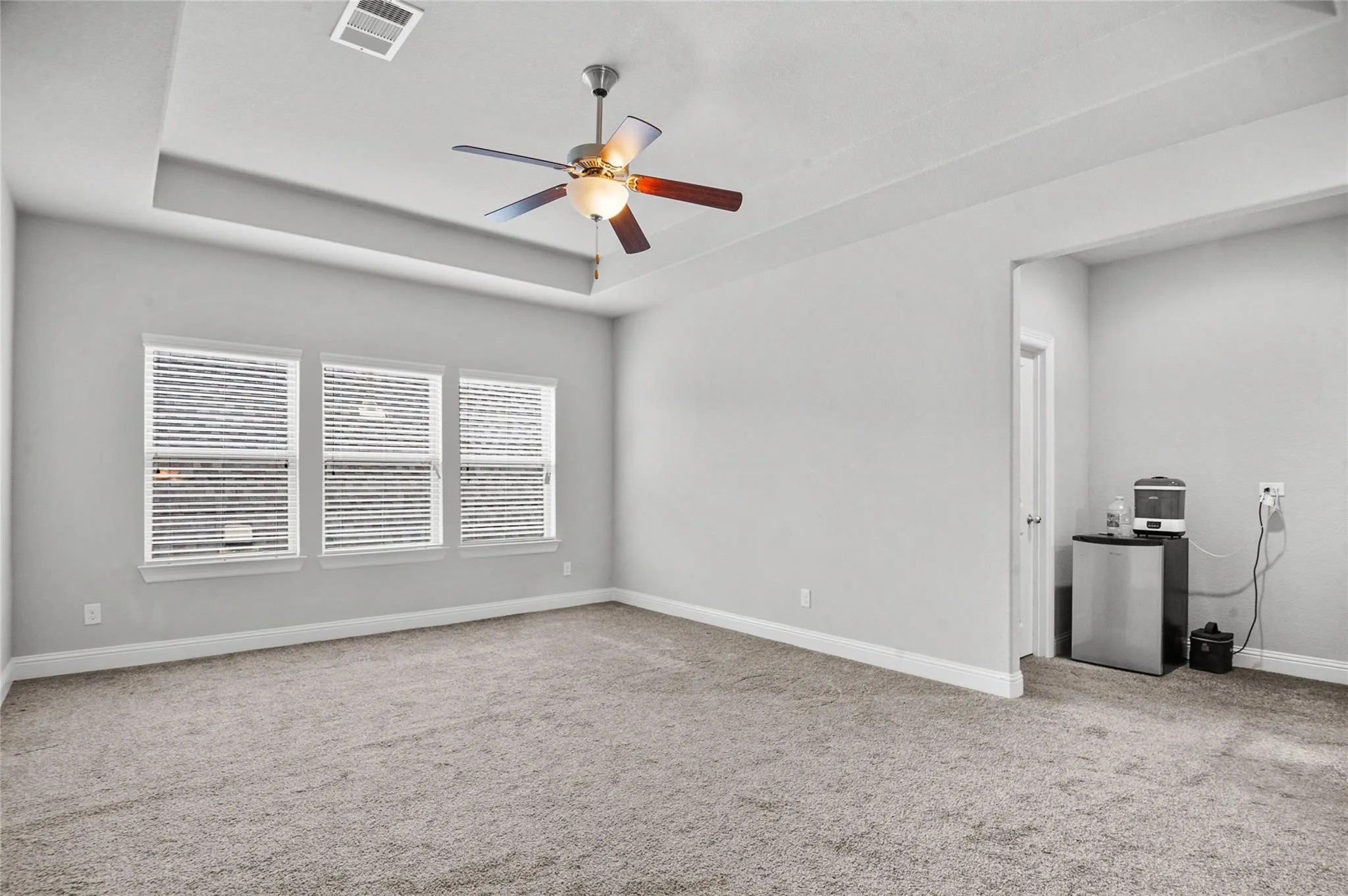 Unfurnished room featuring light colored carpet, ceiling fan, and a tray ceiling