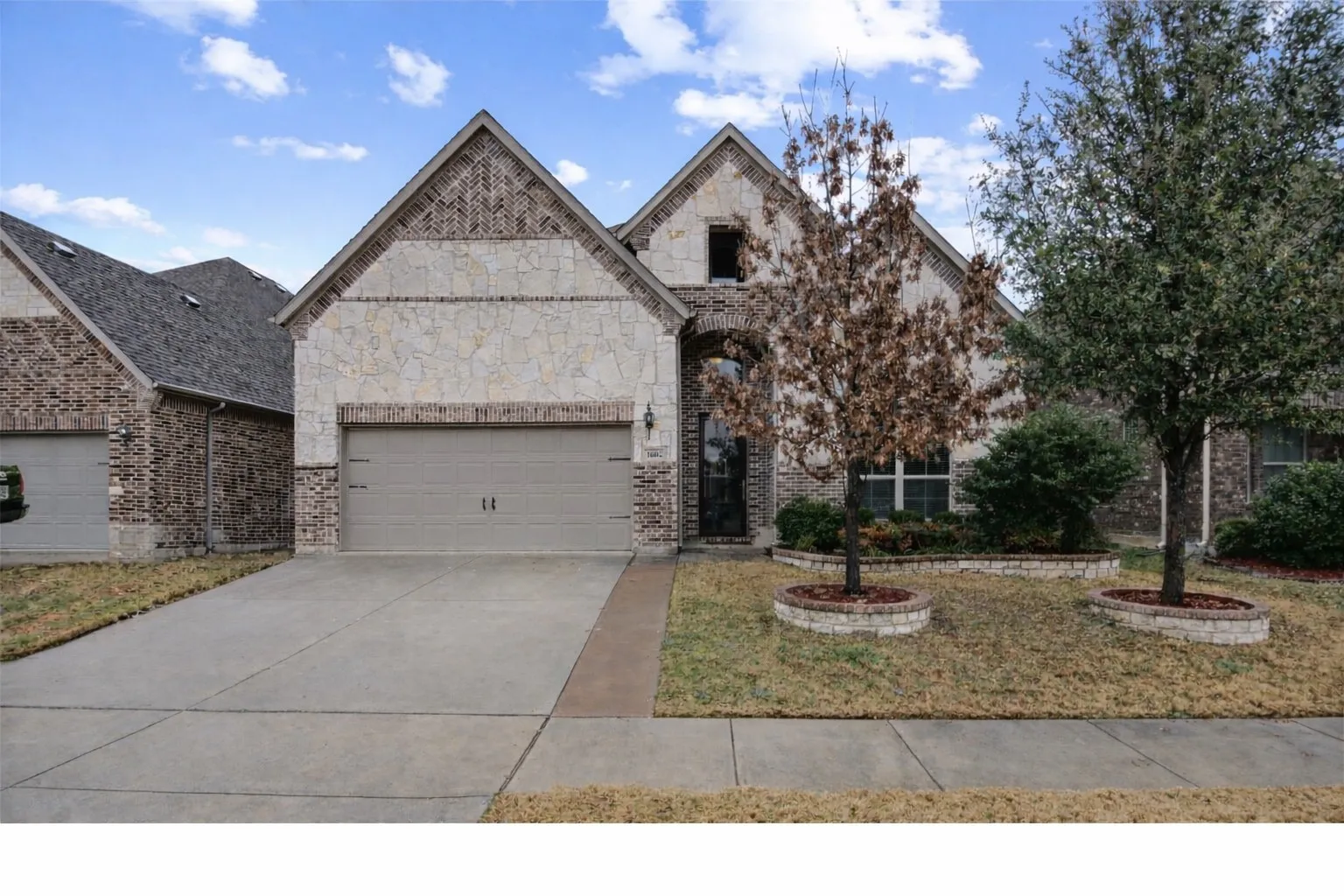 French country inspired facade with an attached garage, driveway, and brick siding
