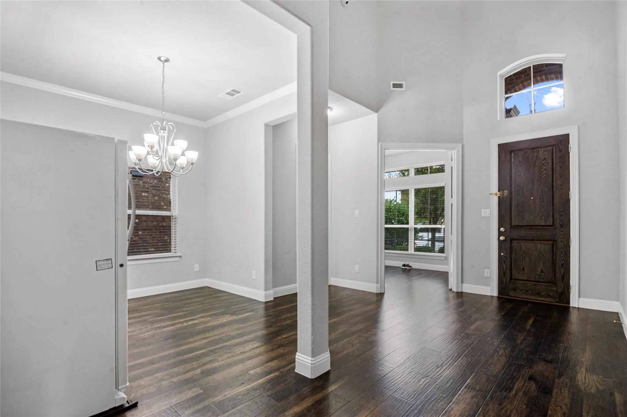 Foyer featuring hanging lights, dark wood finished floors, ornamental molding, and a high ceiling