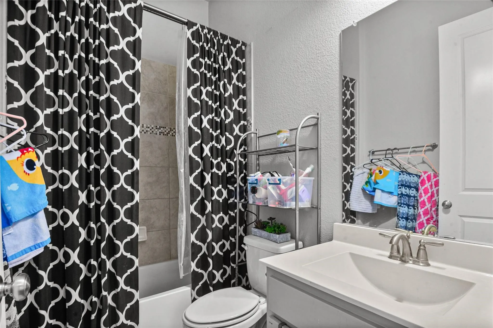 Bathroom featuring a textured wall, shower / bath combo with shower curtain, and vanity