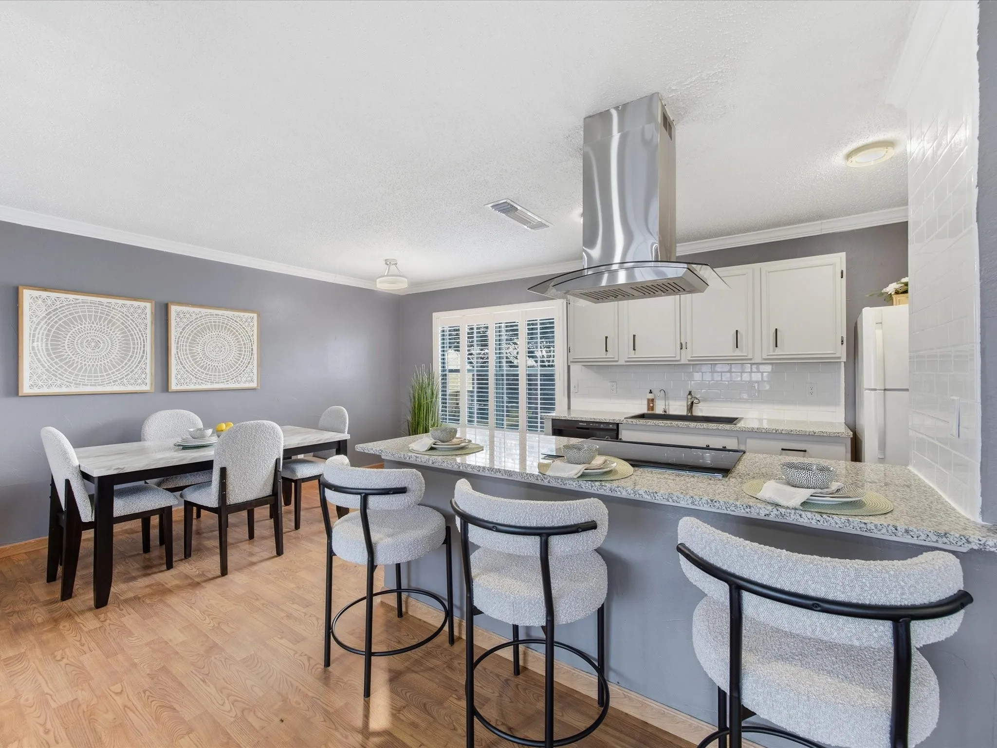Kitchen with island range hood, a kitchen breakfast bar, ornamental molding, light wood-type flooring, and light stone counters