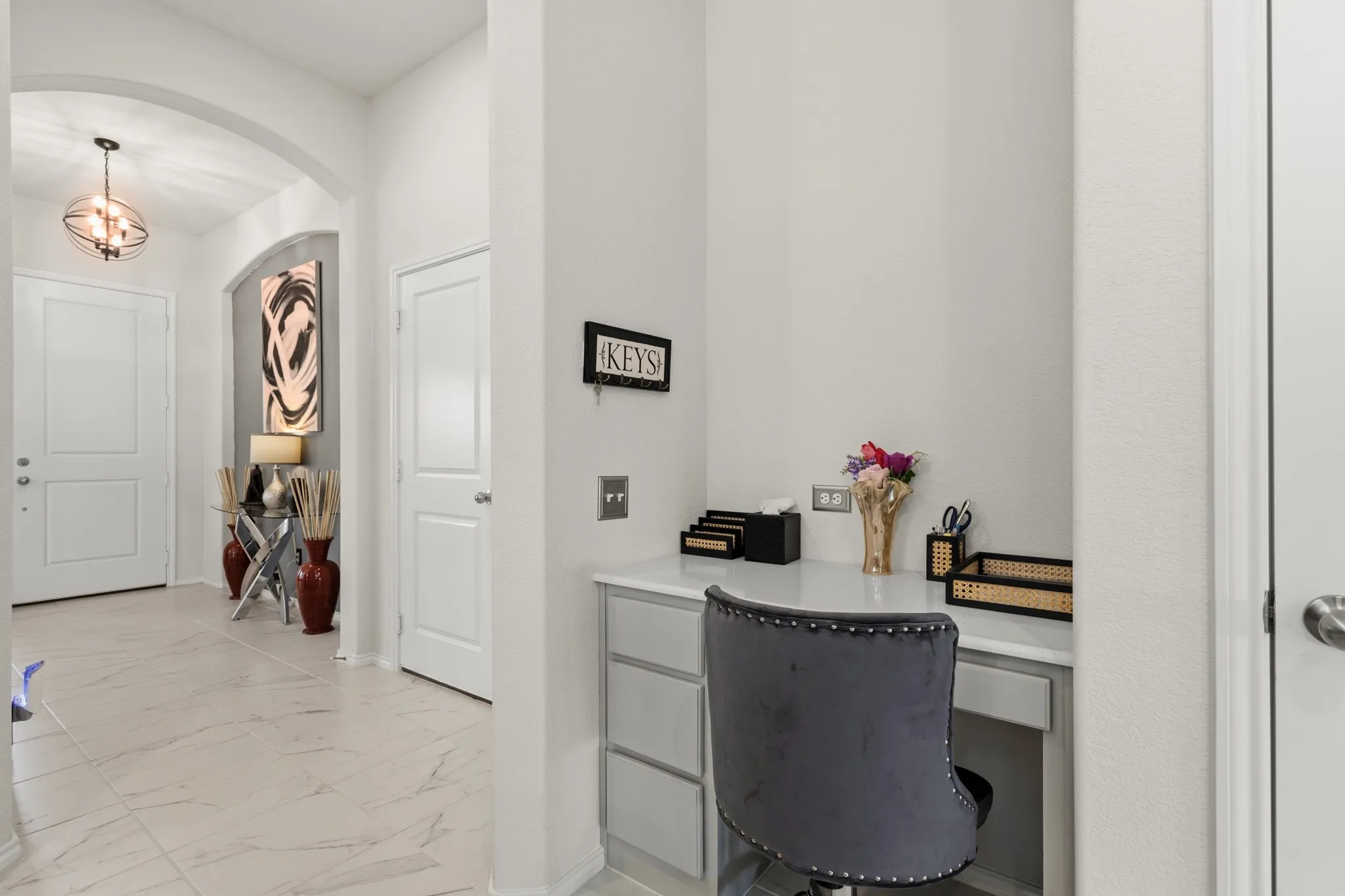 Desk area off of kitchen with arched walkways, built in desk, and light marble finish flooring