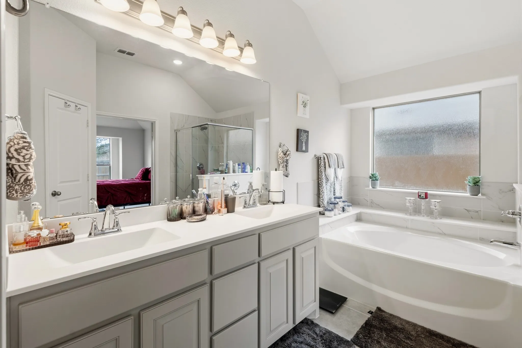 Full bath with ensuite bath, double vanity, vaulted ceiling, plenty of natural light, and a bath