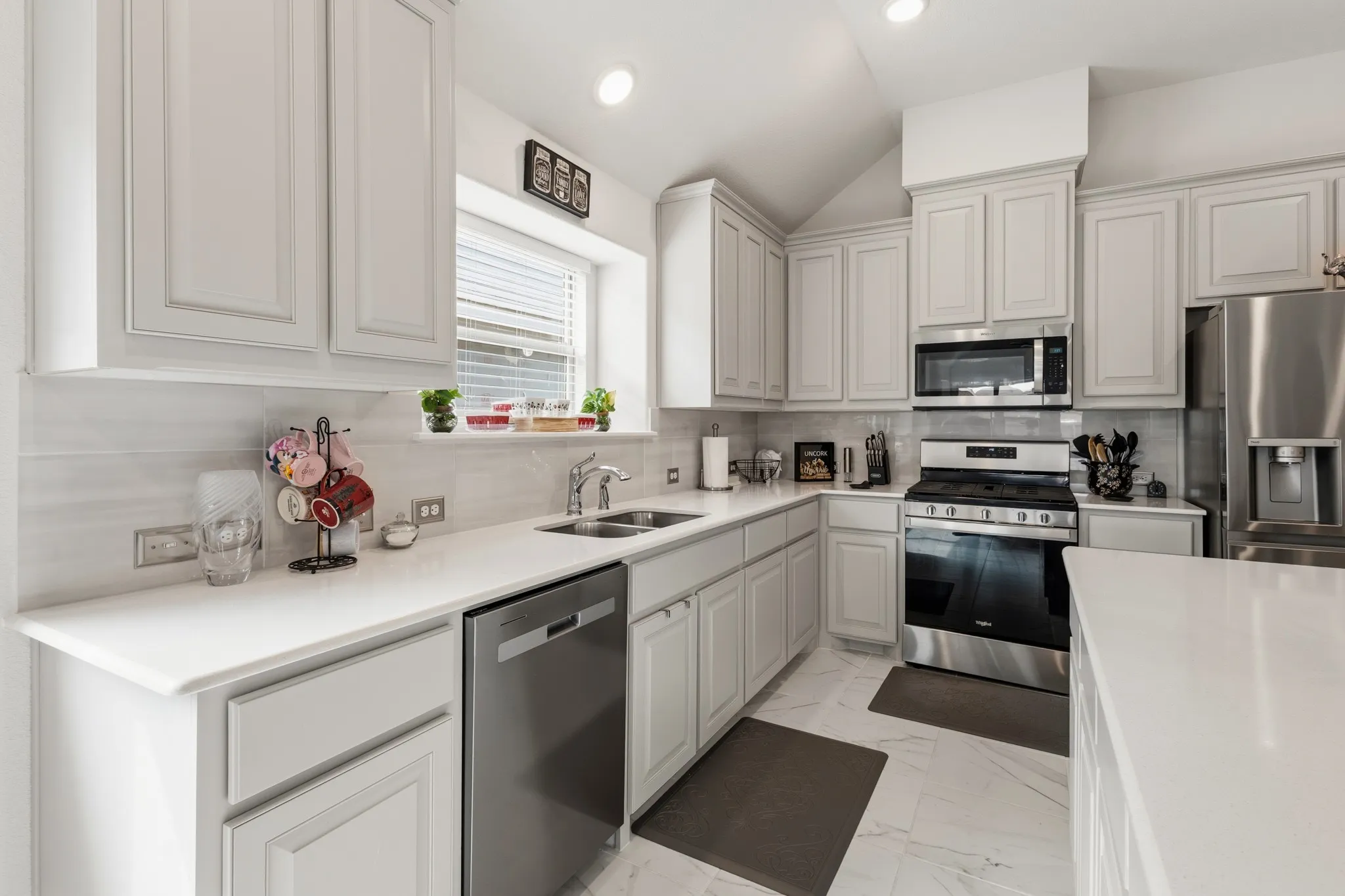 Kitchen with stainless steel appliances, white cabinets, light marble finish flooring, lofted ceiling, and decorative backsplash