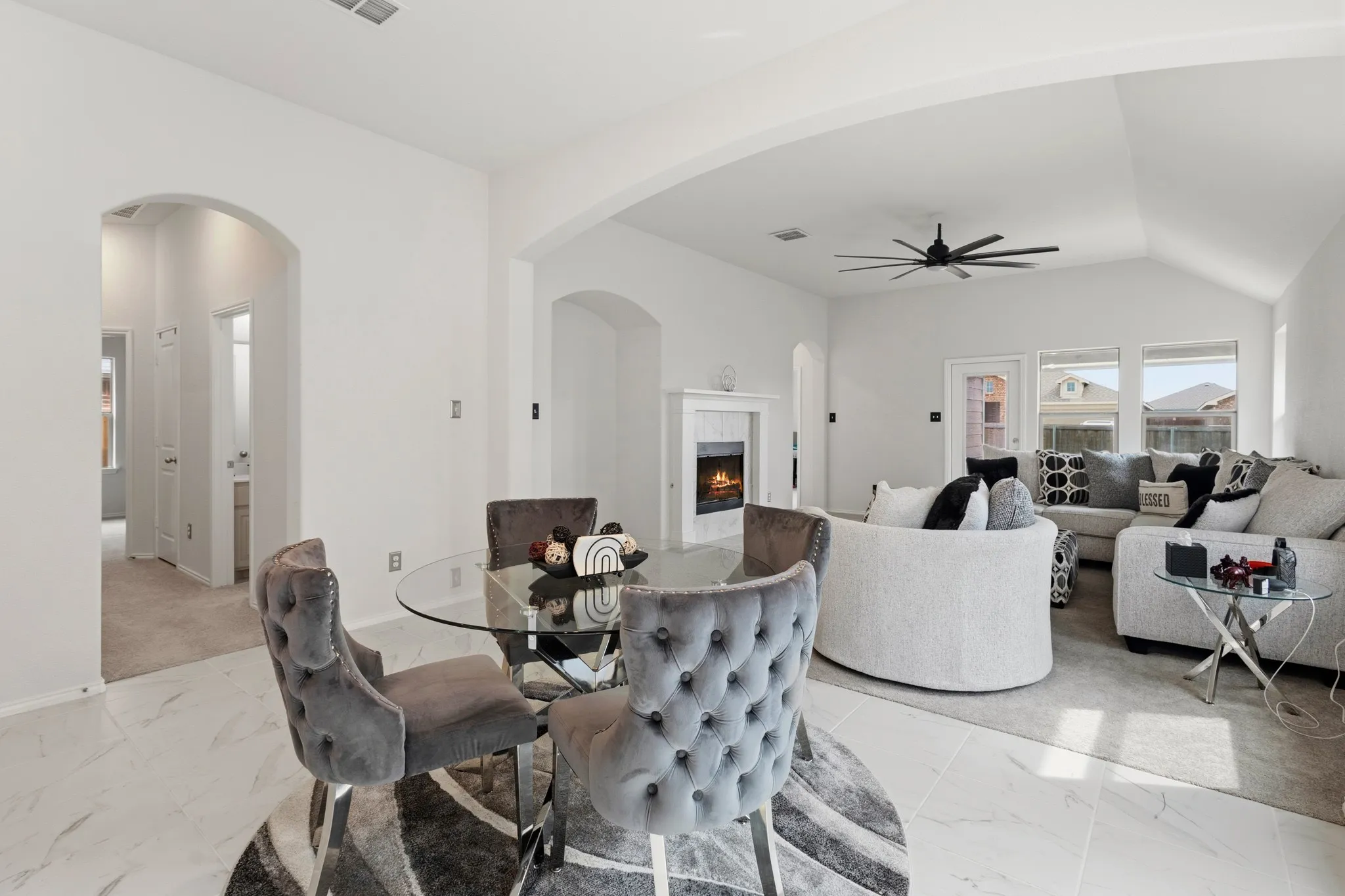 Dining space featuring a warm lit fireplace, vaulted ceiling, ceiling fan, arched walkways, and light marble finish flooring
