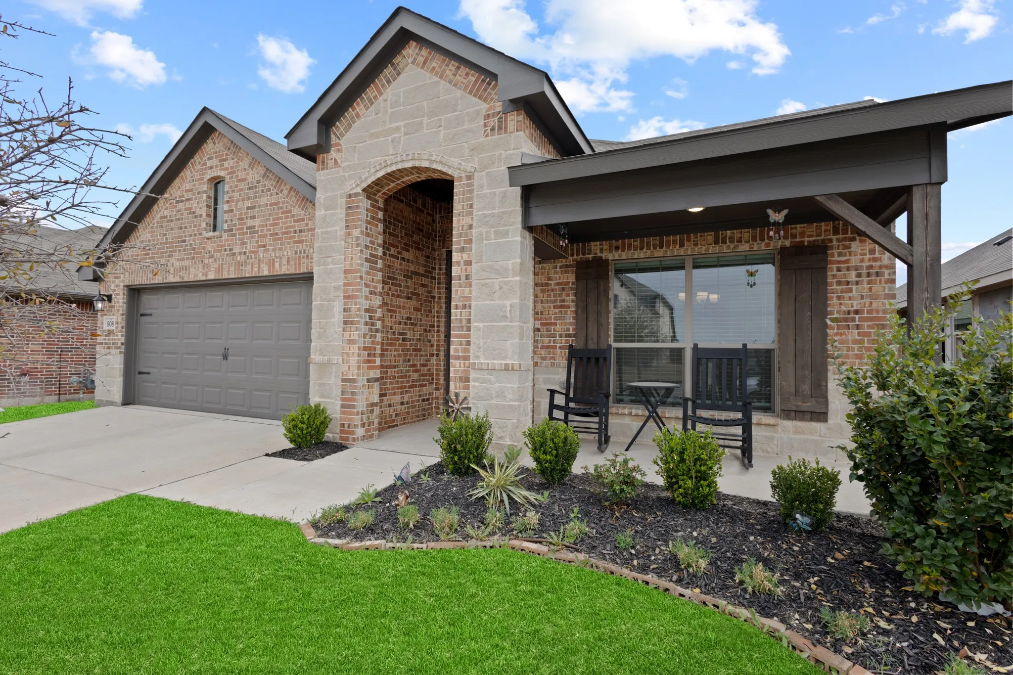 View of front of property with brick siding, driveway, covered porch, a front lawn, and stone siding