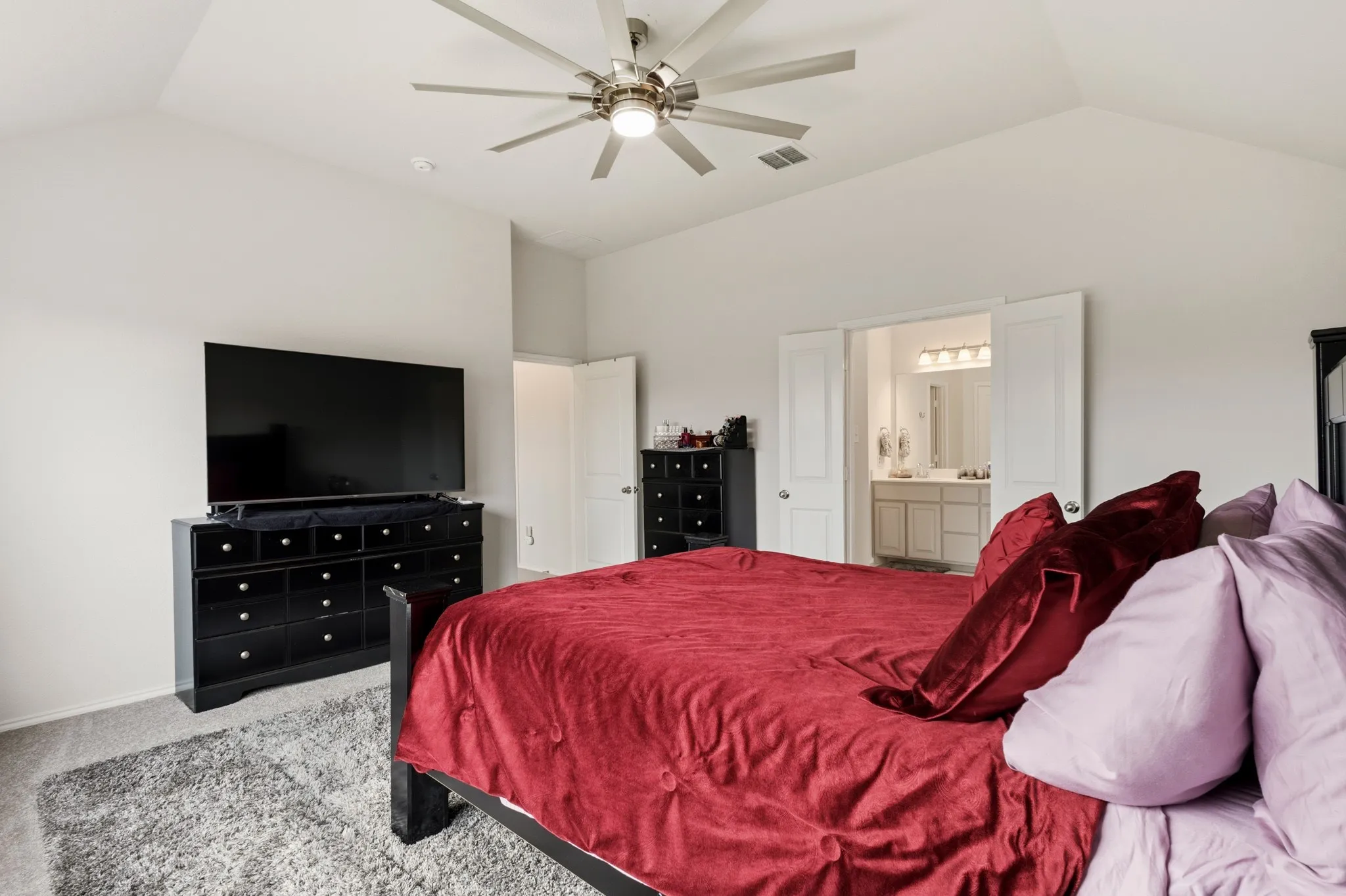 Primary bedroom with light carpet, a ceiling fan, and ensuite bath