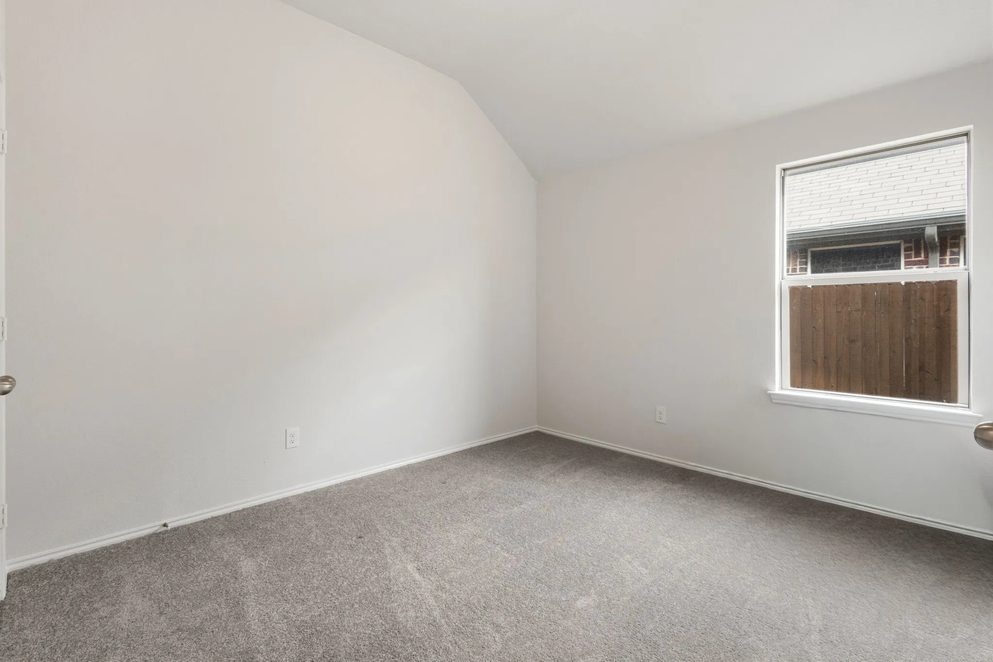 Carpeted spare room featuring lofted ceiling and baseboards