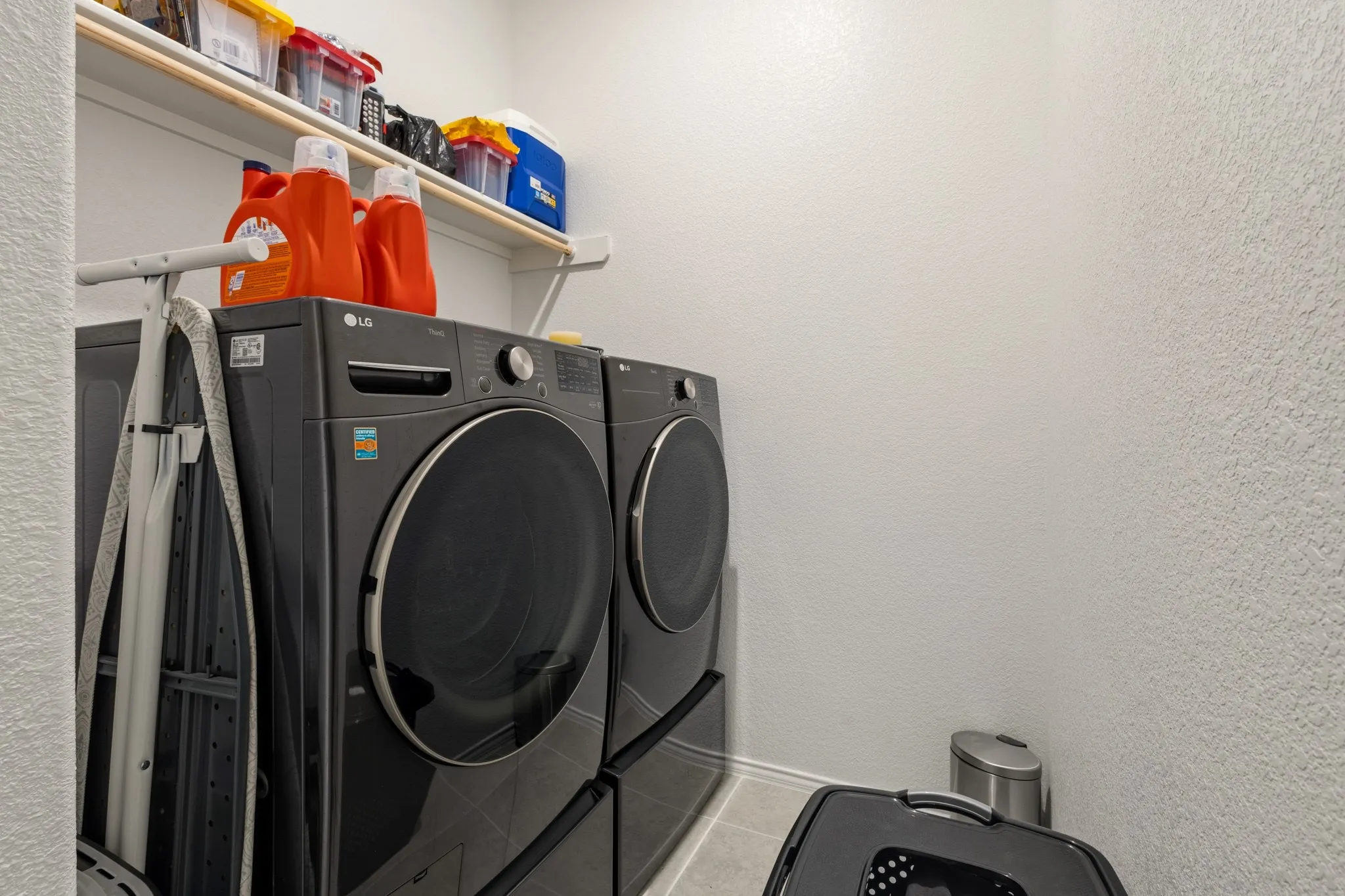 Laundry area with washer and clothes dryer, a textured wall, and light tile patterned floors