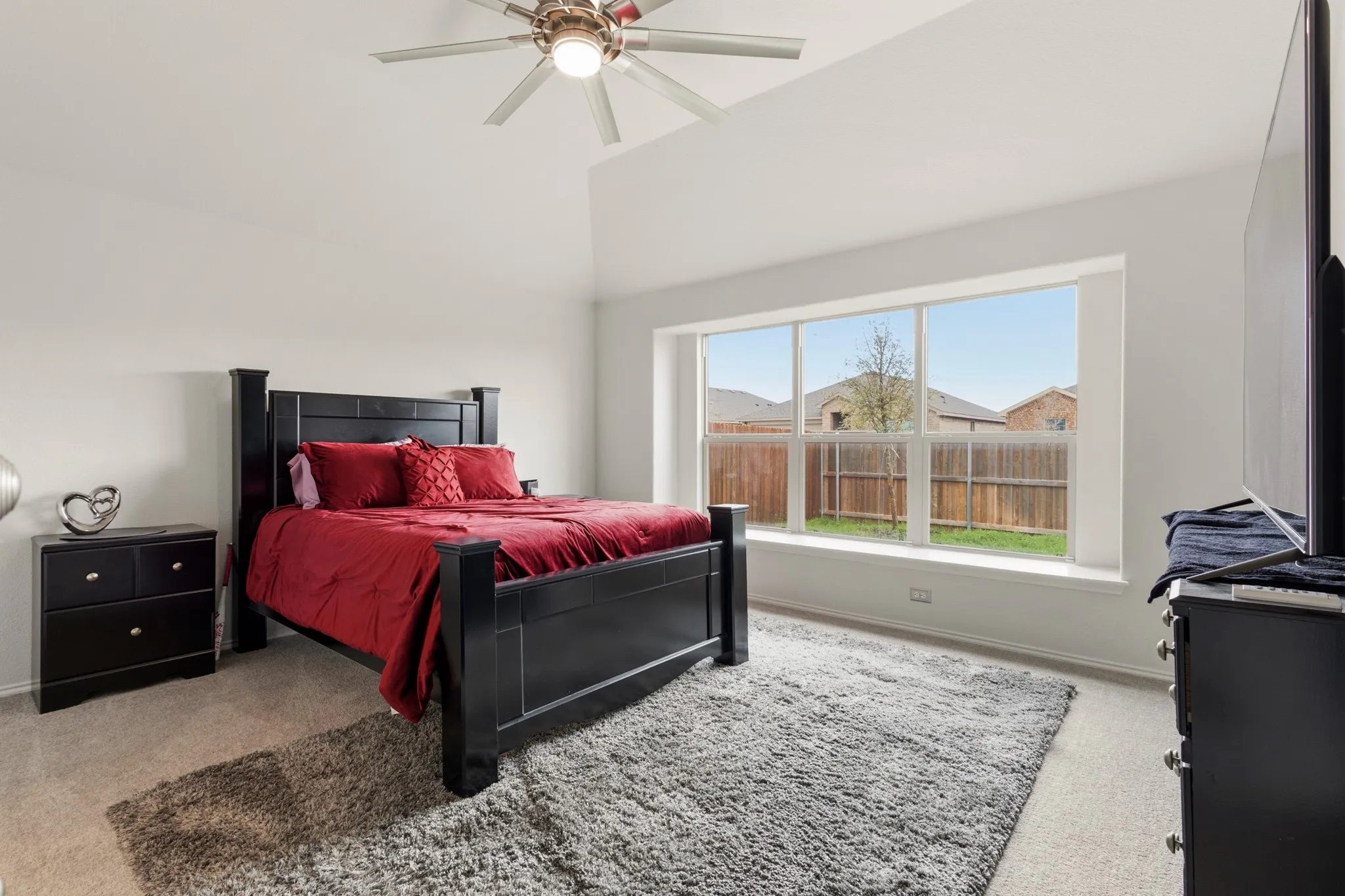 Primary bedroom featuring light carpet, a ceiling fan, and vaulted ceiling