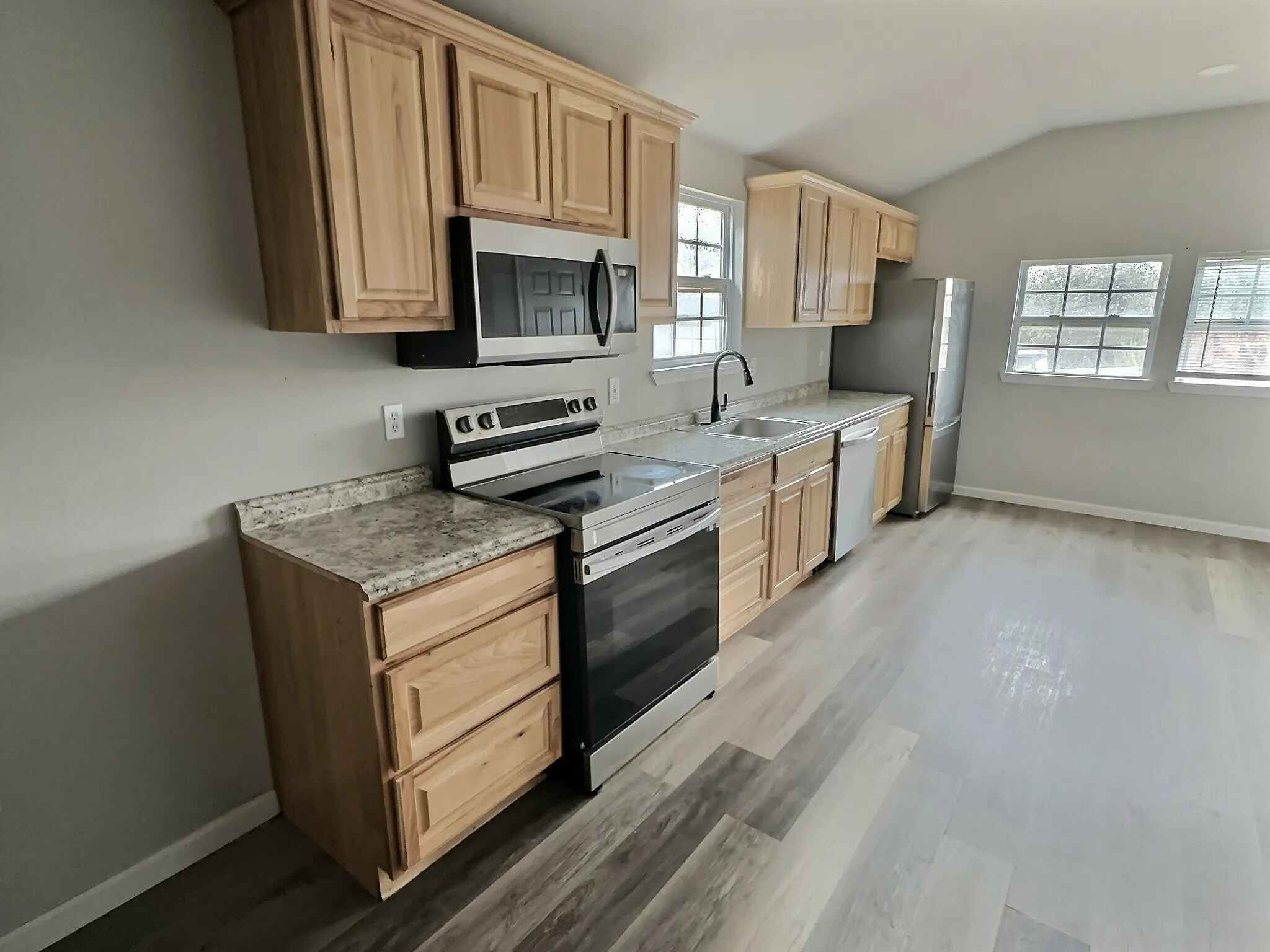 Kitchen with stainless steel appliances, light wood finish cabinetry, light countertops, lofted ceiling, and light wood-type flooring