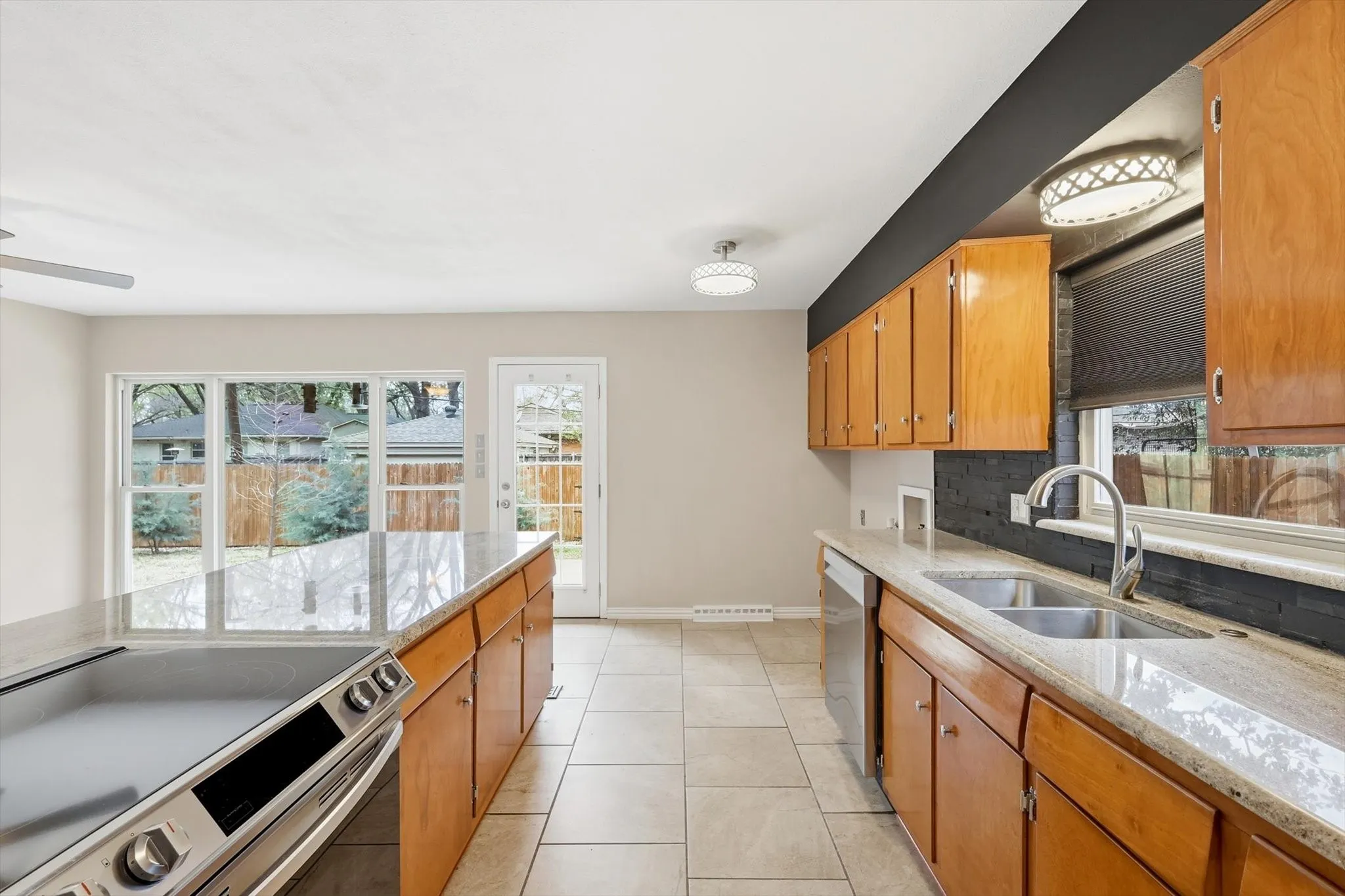 Kitchen with stainless steel appliances, light stone counters, wood finish cabinetry, light tile patterned floors, and tasteful backsplash