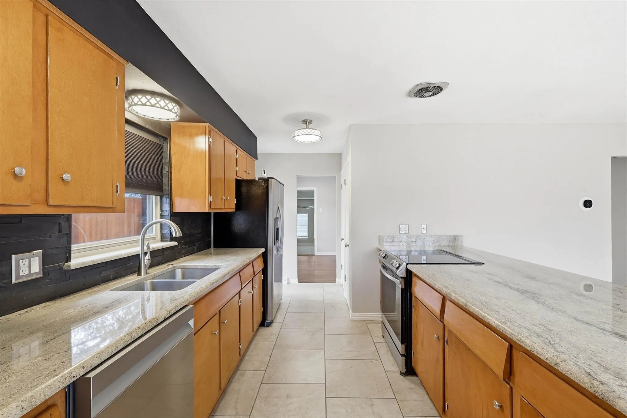 Kitchen with stainless steel appliances, wood finish cabinetry, light stone countertops, and tasteful backsplash