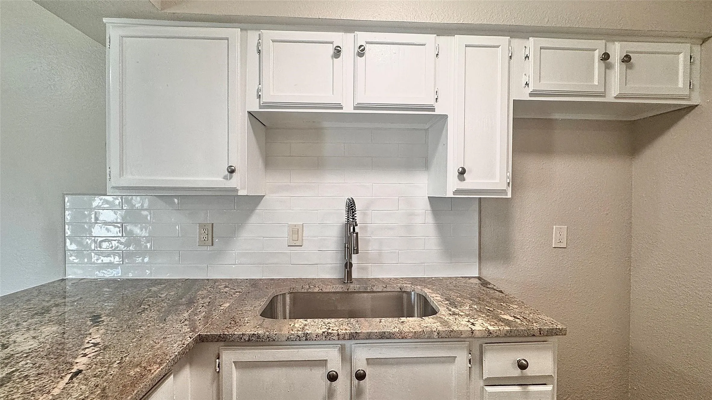 Kitchen featuring a textured wall, dark stone countertops, white cabinets, and tasteful backsplash