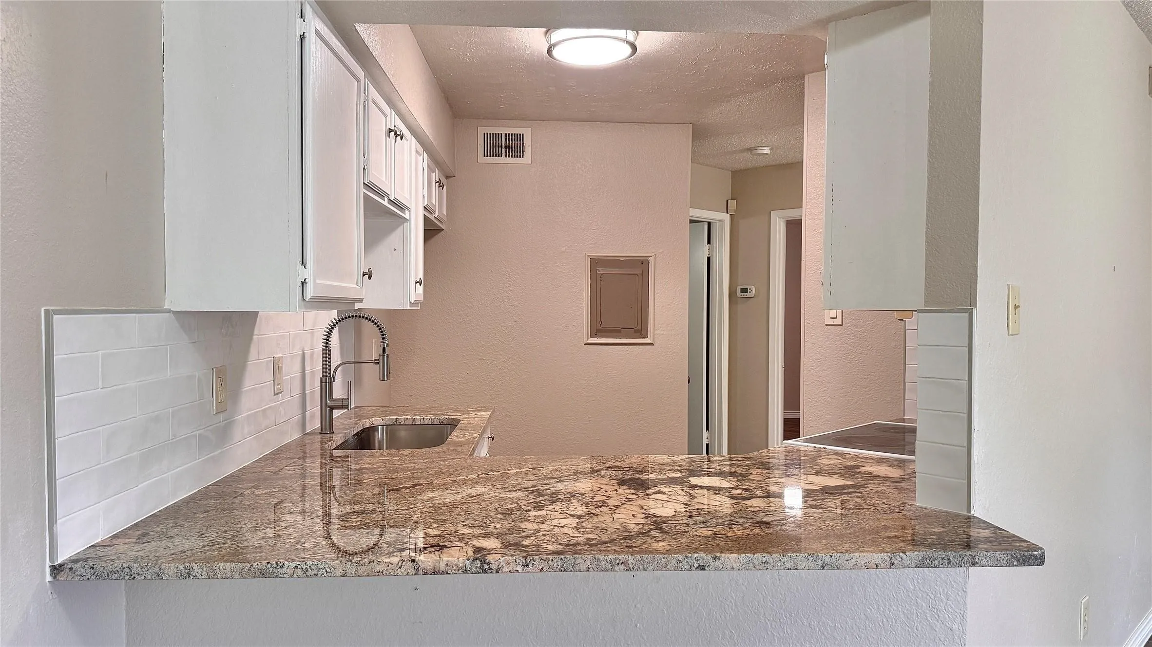 Kitchen featuring white cabinets, light stone counters, a textured wall, and a textured ceiling