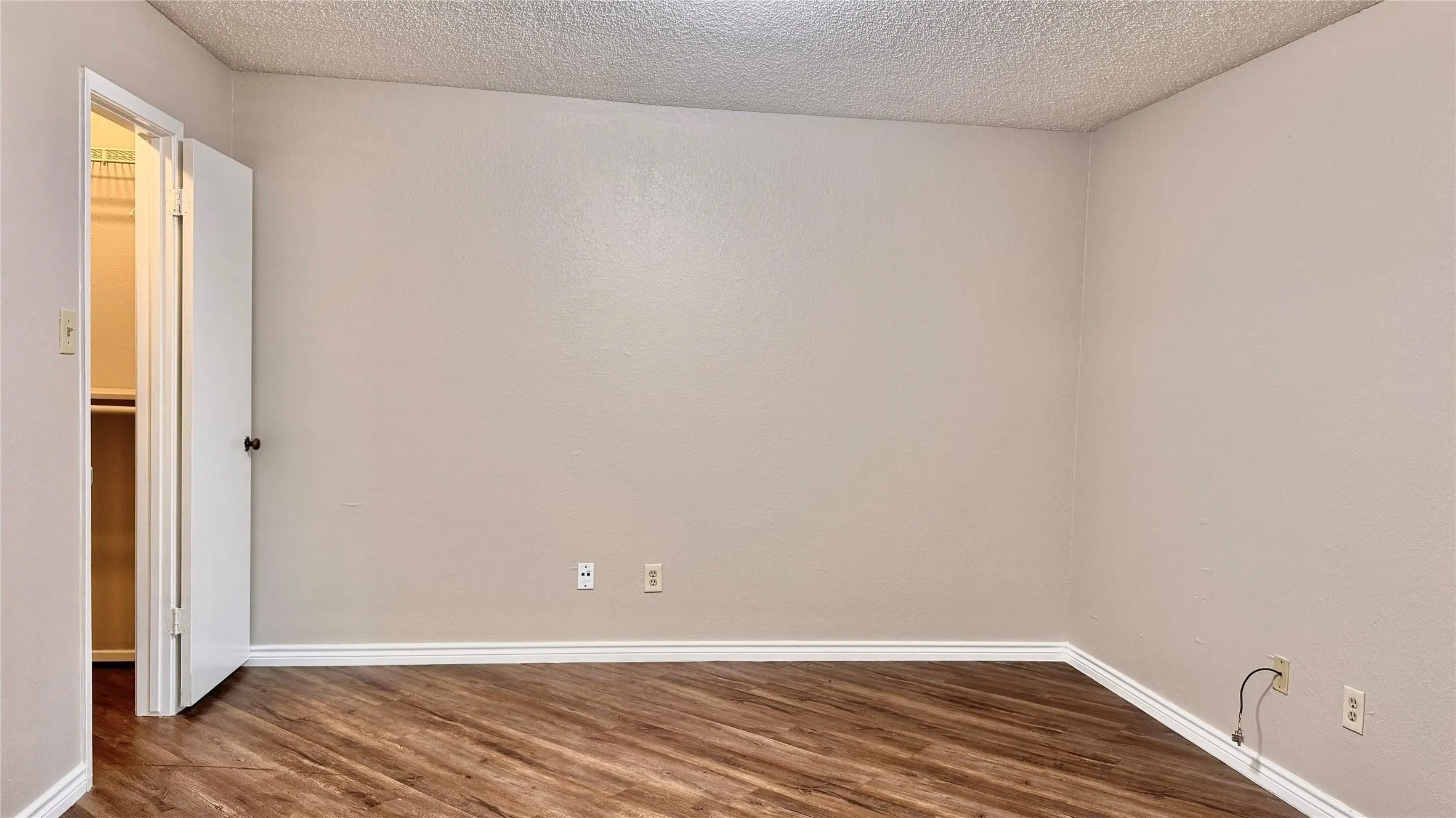Unfurnished room featuring dark wood-type flooring and a textured ceiling