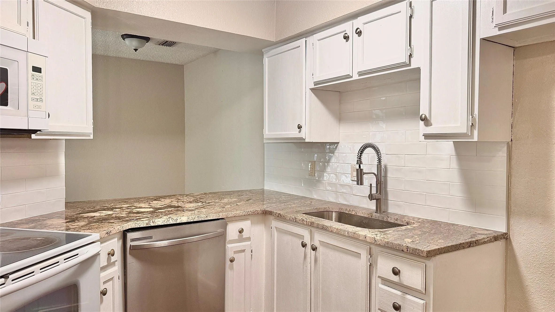Kitchen with white appliances, light stone counters, white cabinetry, and tasteful backsplash