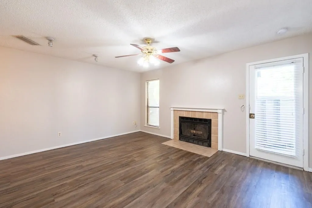Unfurnished living room with dark wood-type flooring, a ceiling fan, a textured ceiling, and a tile fireplace