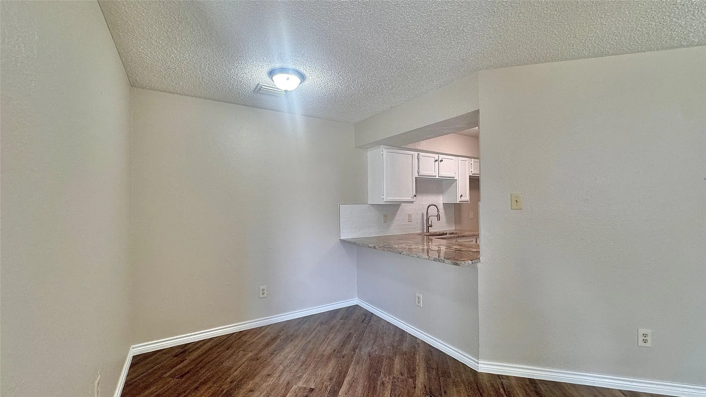 Unfurnished dining area featuring a textured ceiling and dark wood-type flooring