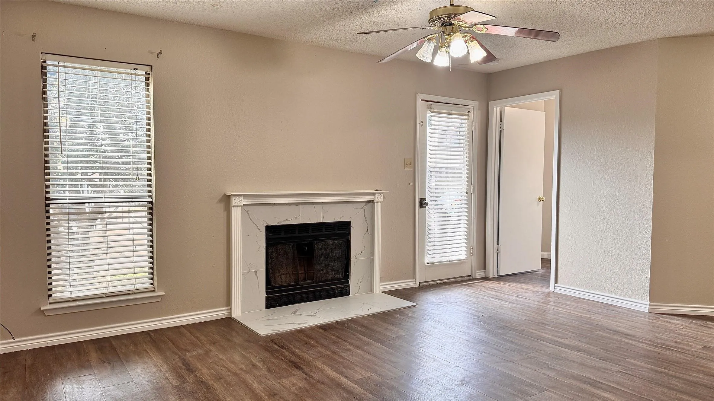 Unfurnished living room featuring ceiling fan, a textured ceiling, dark wood-type flooring, and a high end fireplace