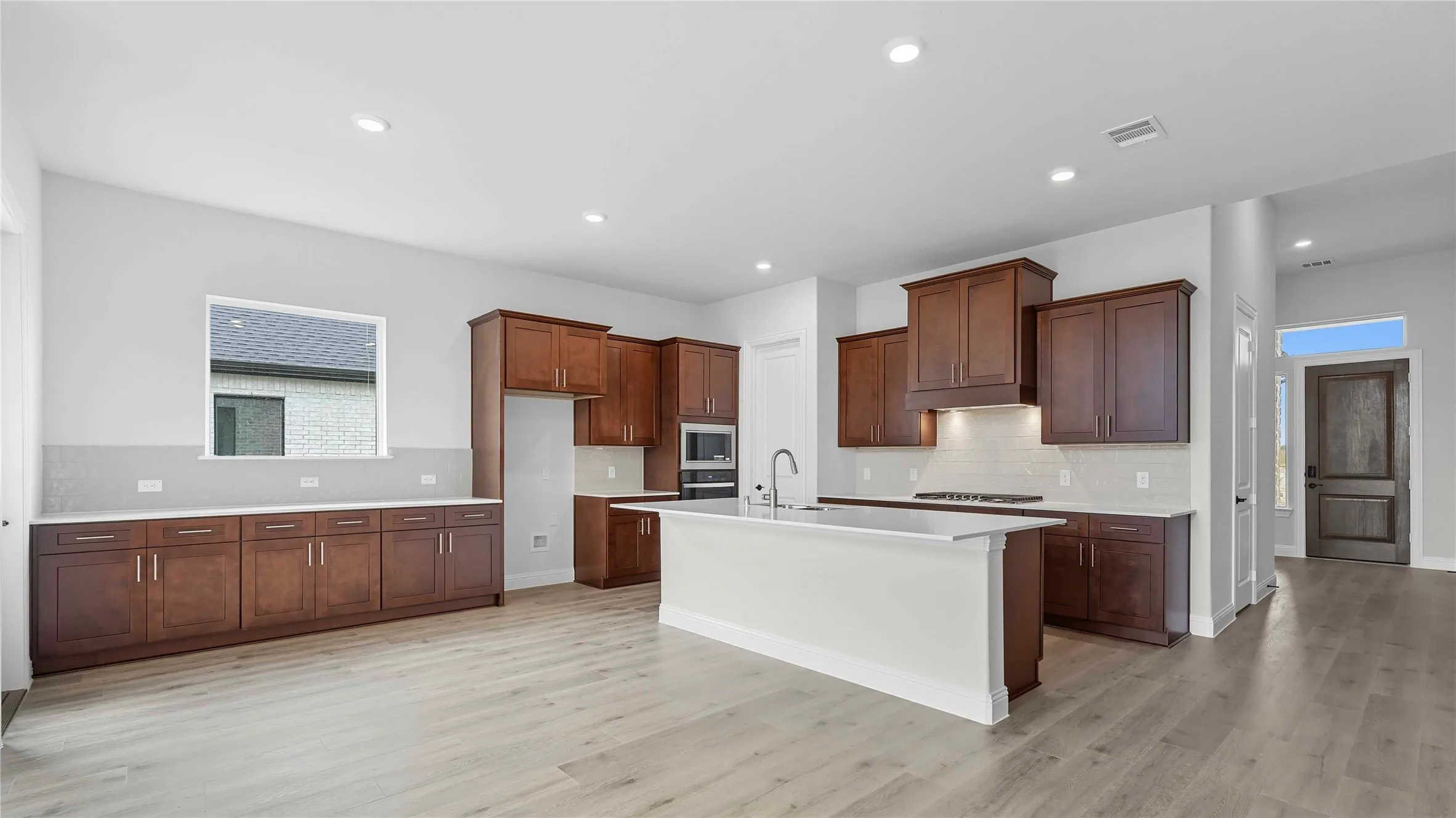 Open-concept kitchen featuring an expansive center island, extensive cabinetry with dark wood finishes, light-toned countertops, and wood-finish flooring