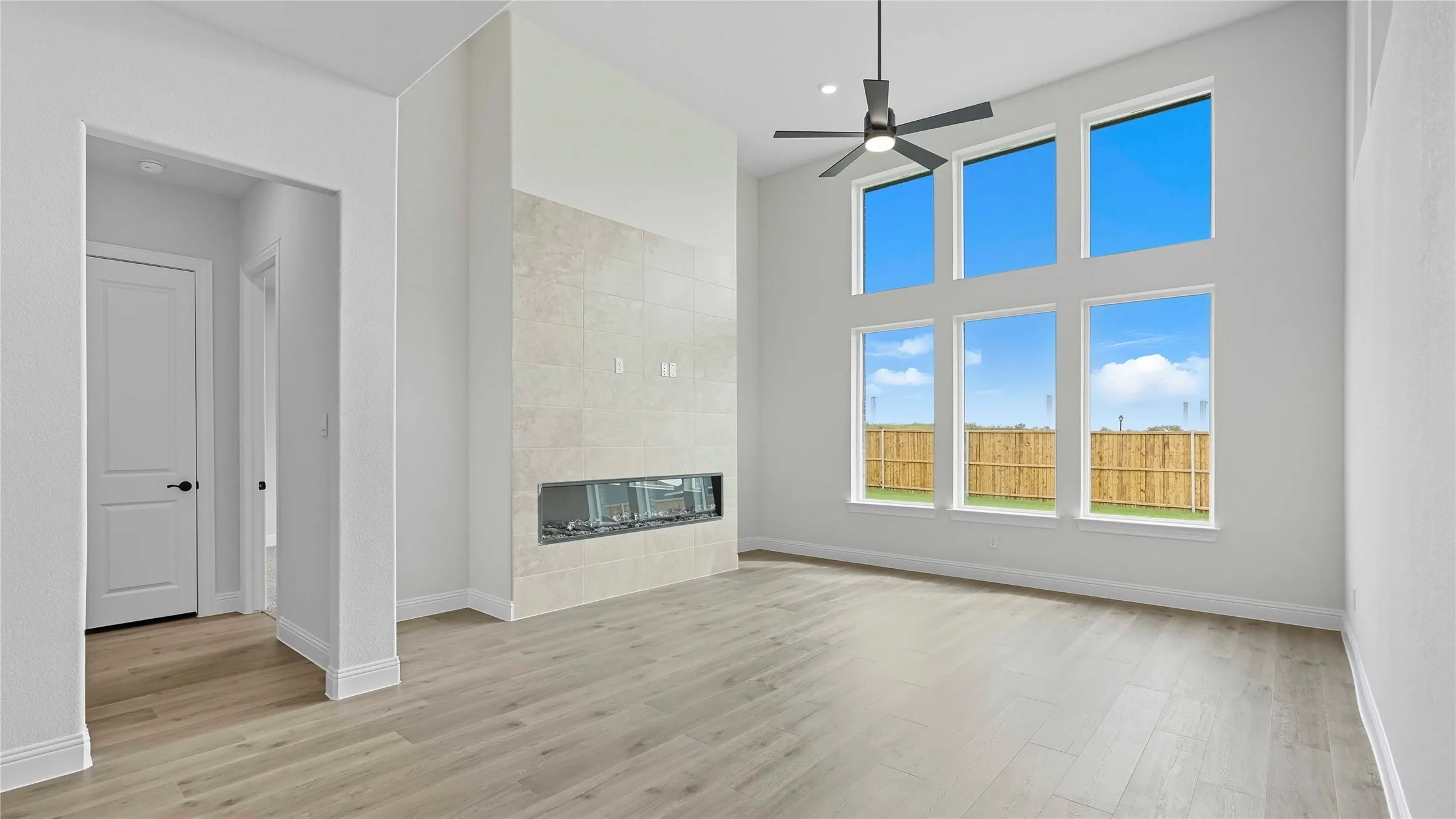 Spacious living area featuring a tall ceiling, a linear fireplace with a light-toned tile surround, and a ceiling fan