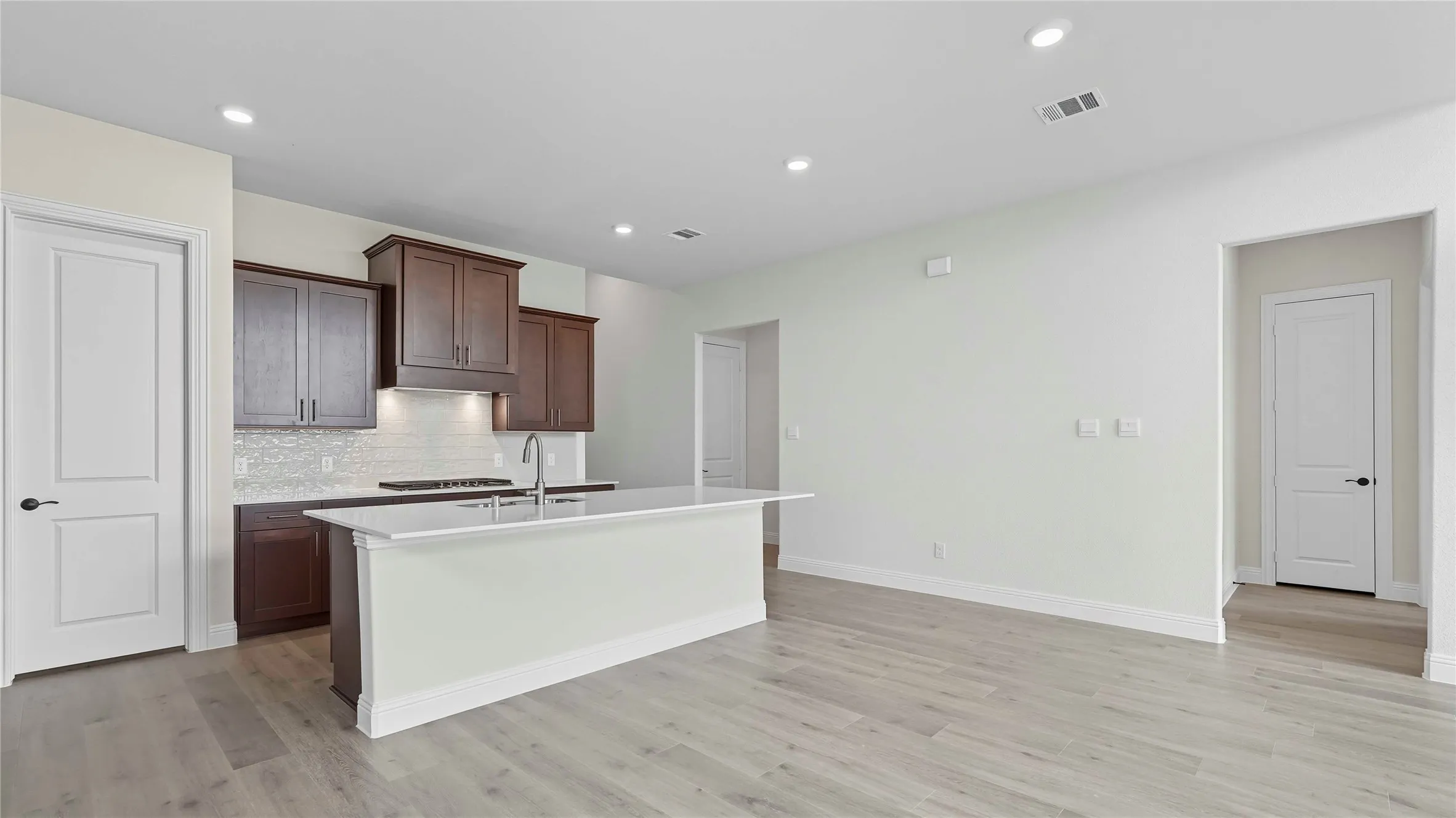 Open-concept kitchen featuring an island with a breakfast bar, dark wood cabinetry, a tile backsplash, and light wood-finish flooring