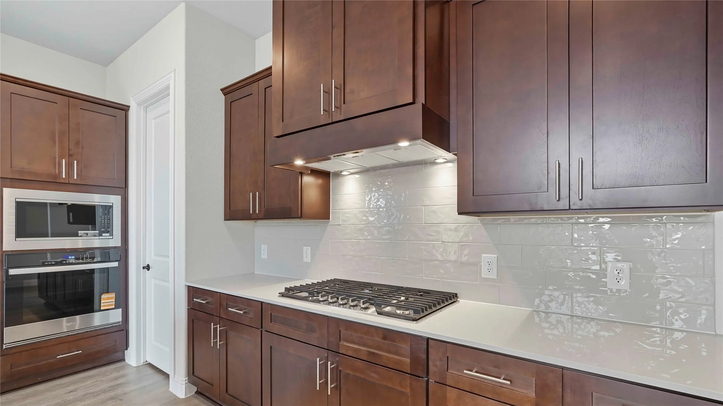 Kitchen featuring dark wood-finish cabinetry, light-toned countertops, a stainless steel gas cooktop, a built-in microwave, and a wall oven