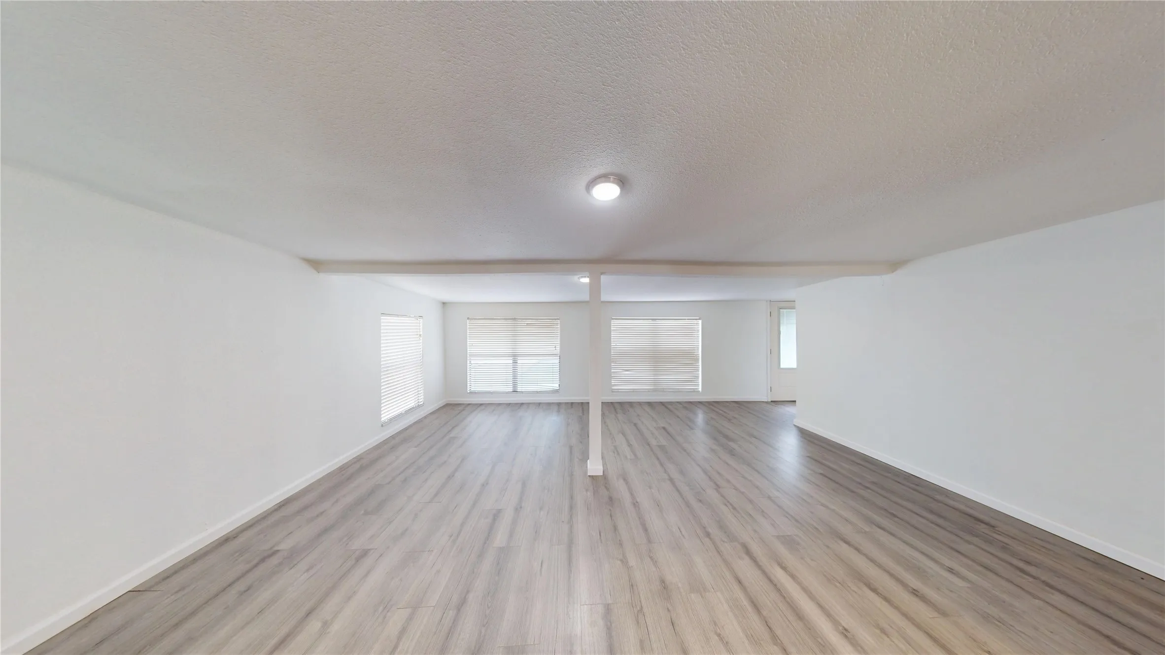 Empty room with light wood-type flooring, a textured ceiling, and beam ceiling