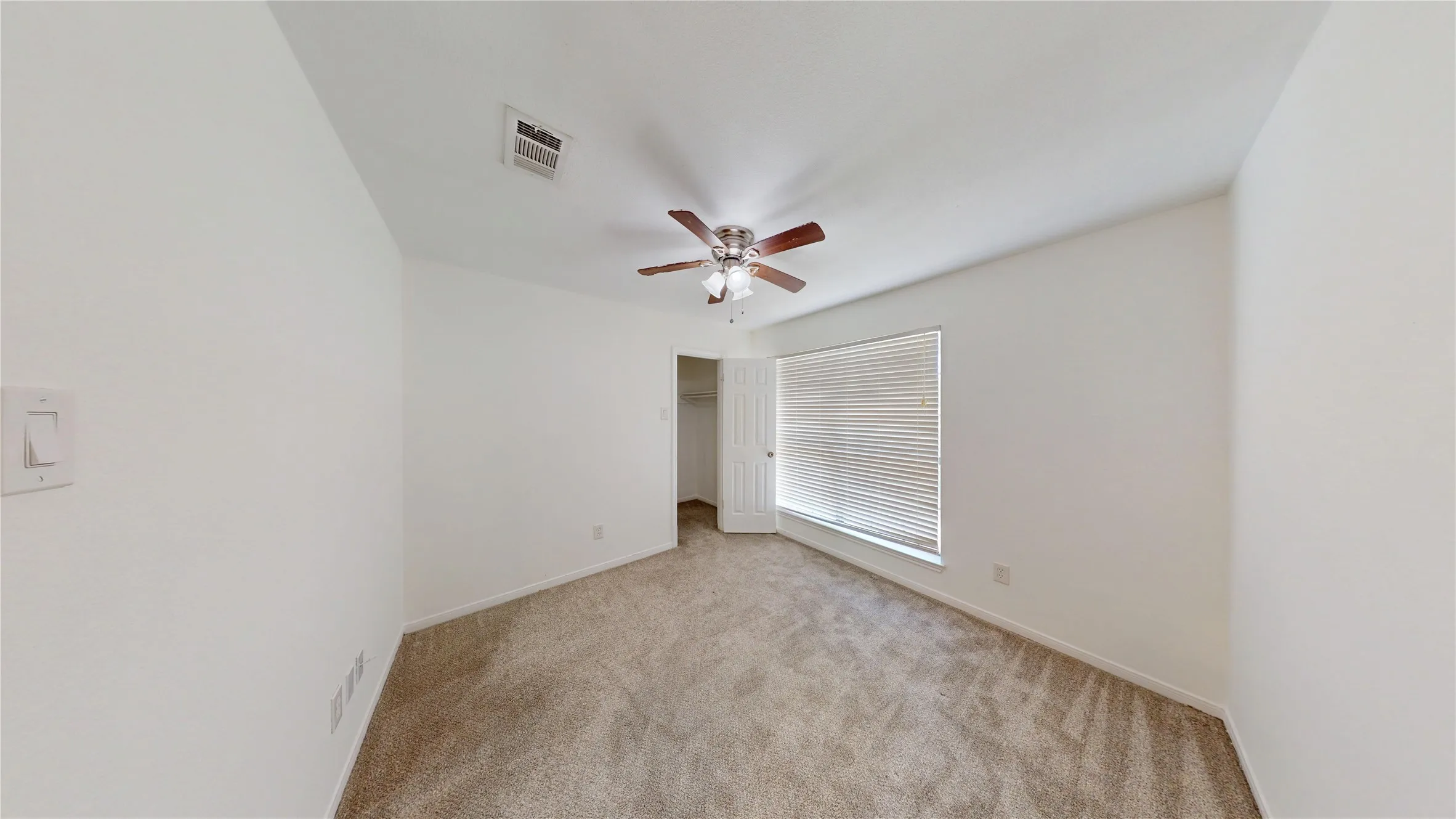 Unfurnished bedroom featuring a walk in closet, light carpet, and ceiling fan