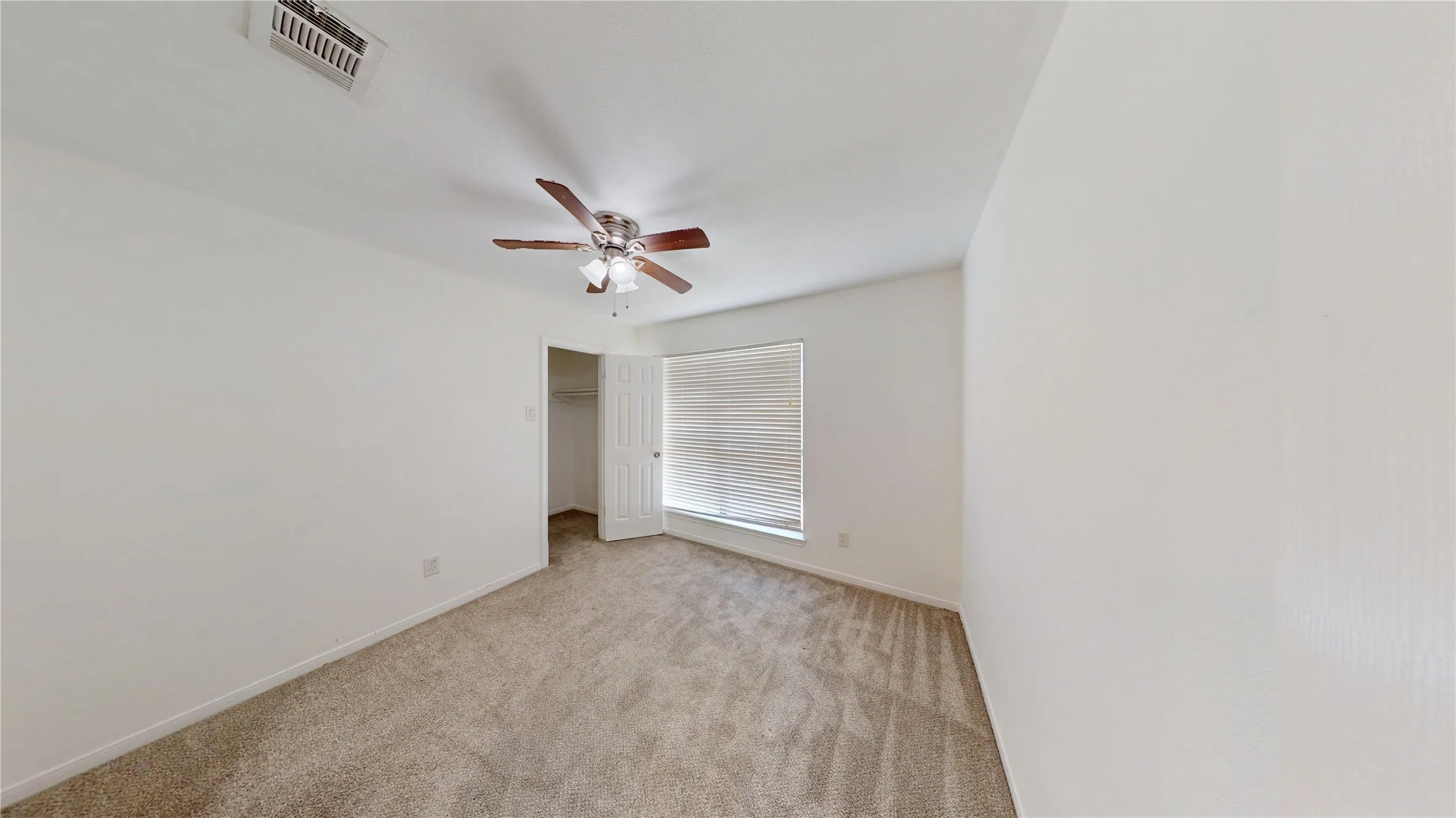Unfurnished bedroom with a walk in closet, light carpet, and a ceiling fan