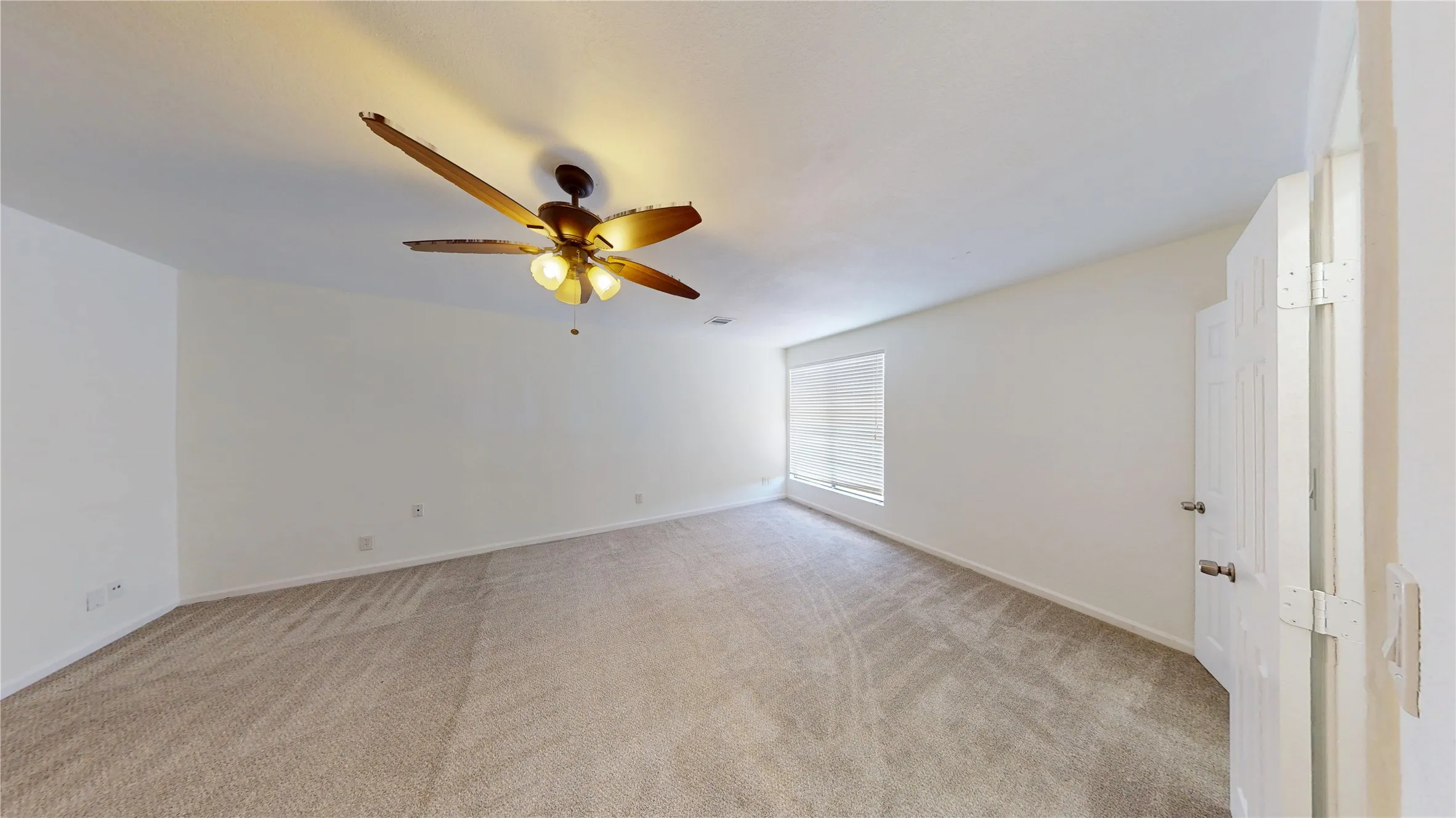 Empty room with light colored carpet and a ceiling fan