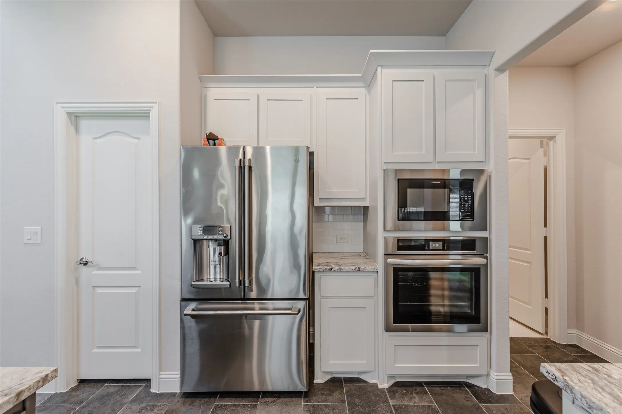 Kitchen featuring stainless steel appliances, white cabinets, light stone counters, and decorative backsplash
