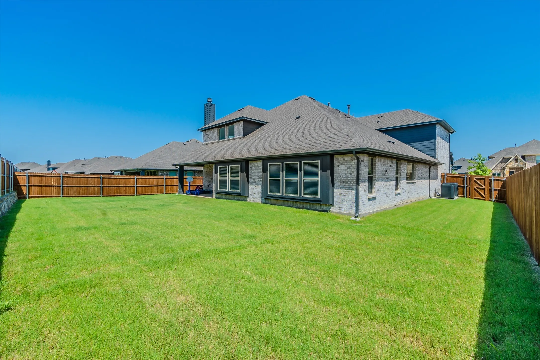 Rear view of property featuring a chimney, a fenced backyard, brick siding, a gate, and roof with shingles