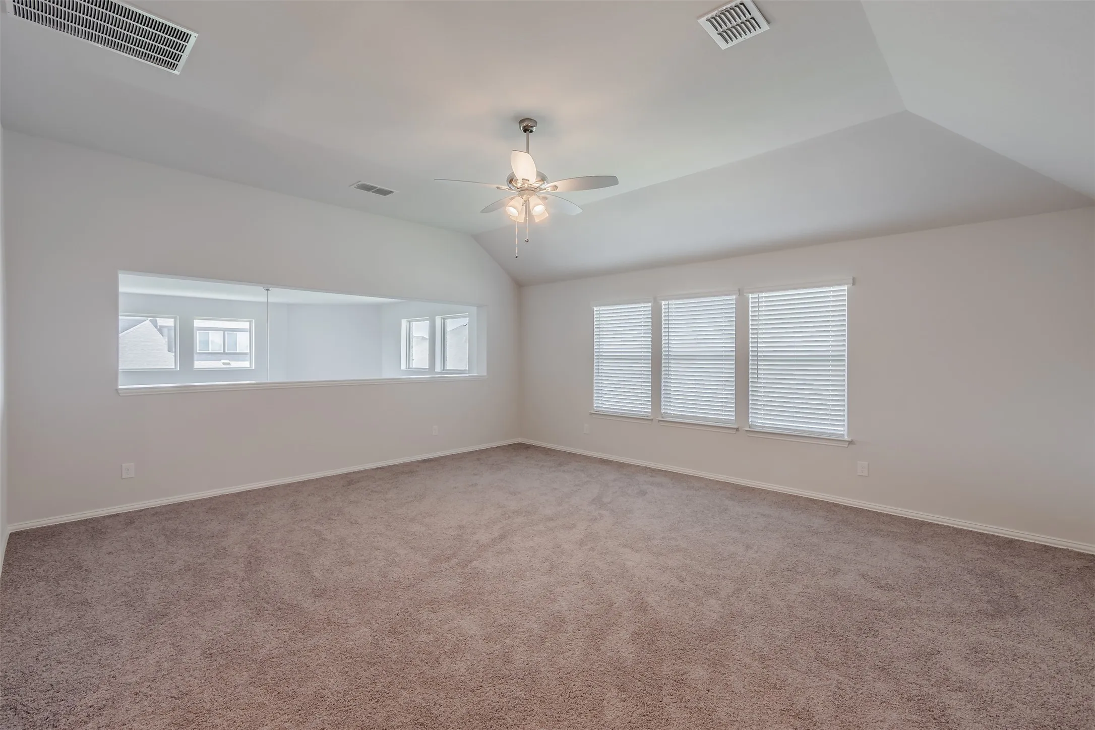 Carpeted empty room featuring vaulted ceiling and ceiling fan