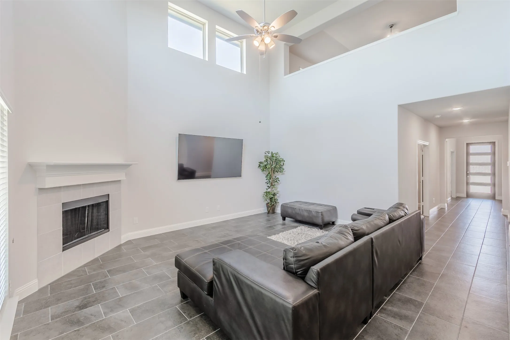 Living room featuring ceiling fan, a tile fireplace, a high ceiling, and tile patterned floors