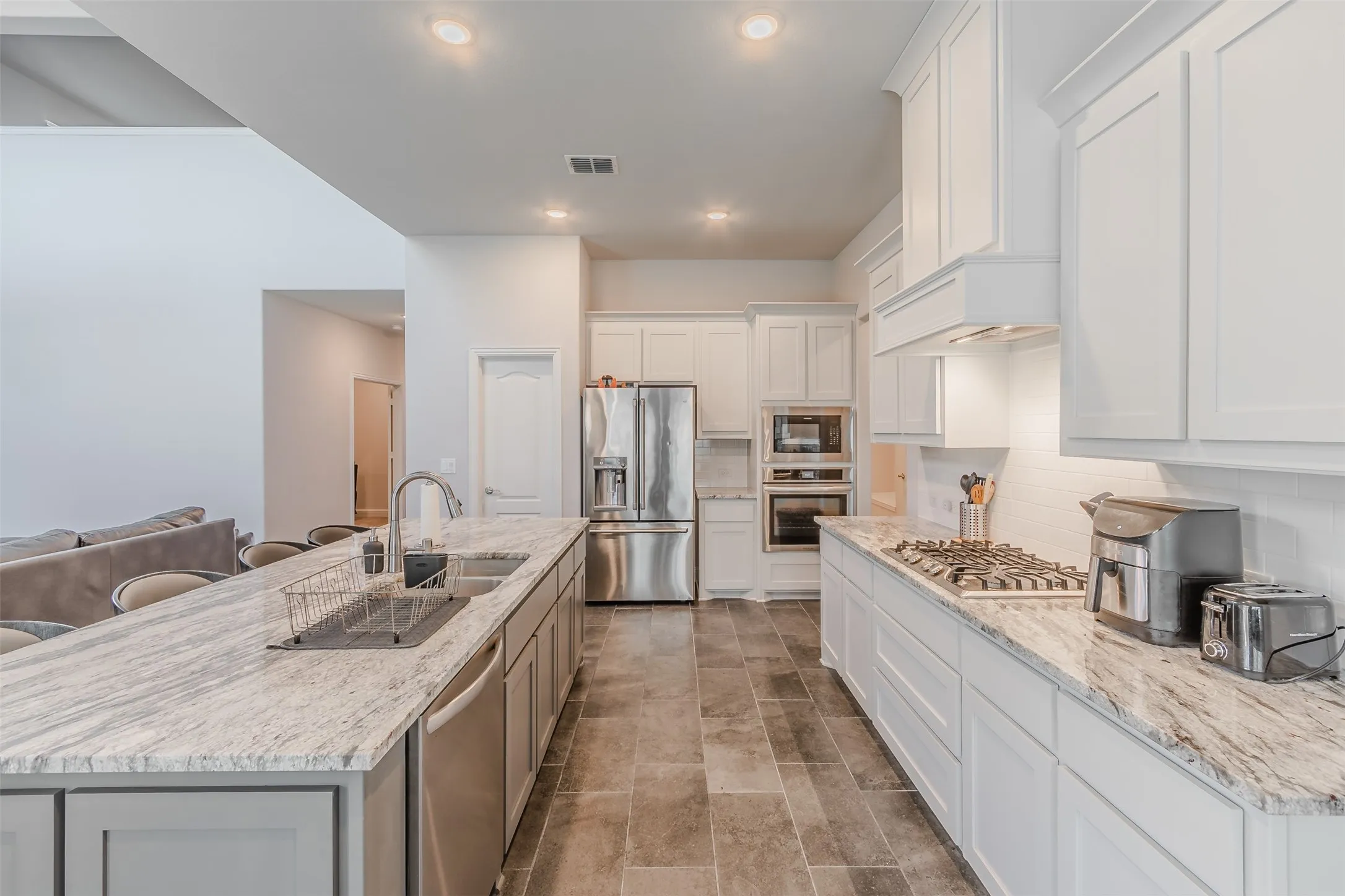 Dual tone kitchen featuring tasteful backsplash, stainless steel appliances, a large island, light stone counters, and recessed lighting