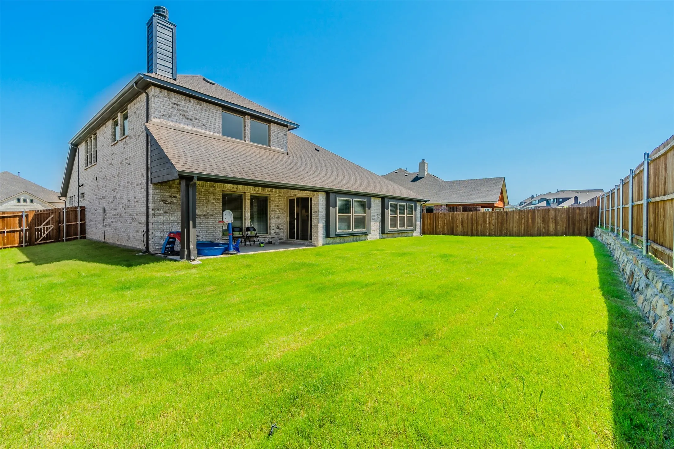 Back of house with brick siding, a fenced backyard, a patio area, a chimney, and roof with shingles