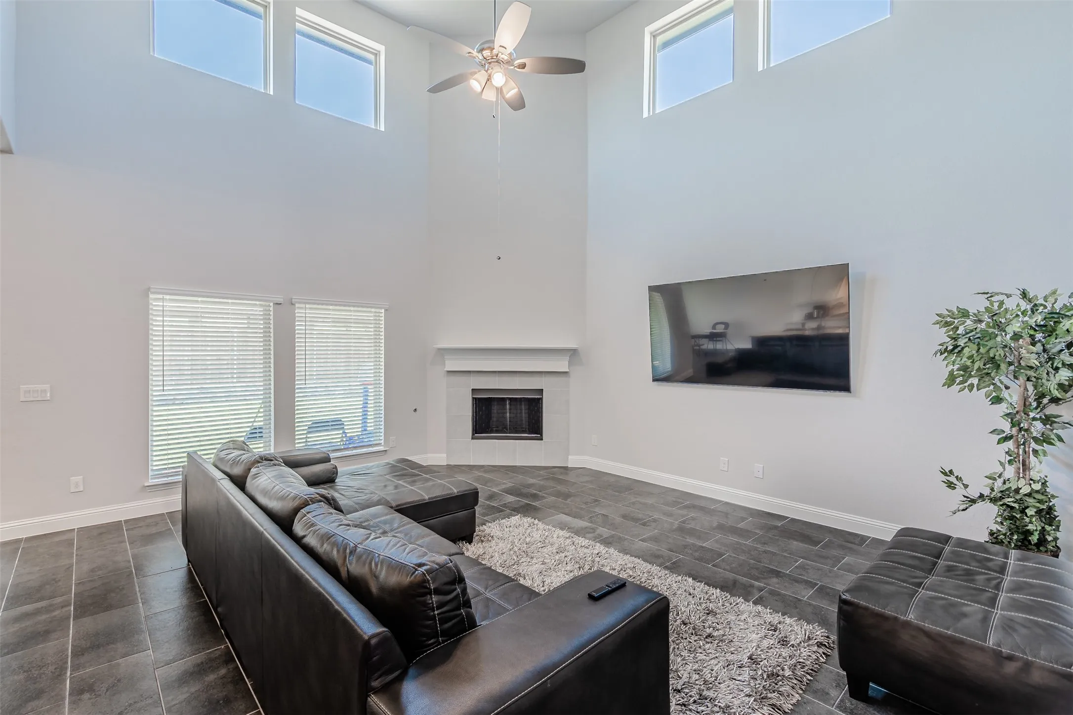 Living room with a tiled fireplace, a ceiling fan, and a high ceiling