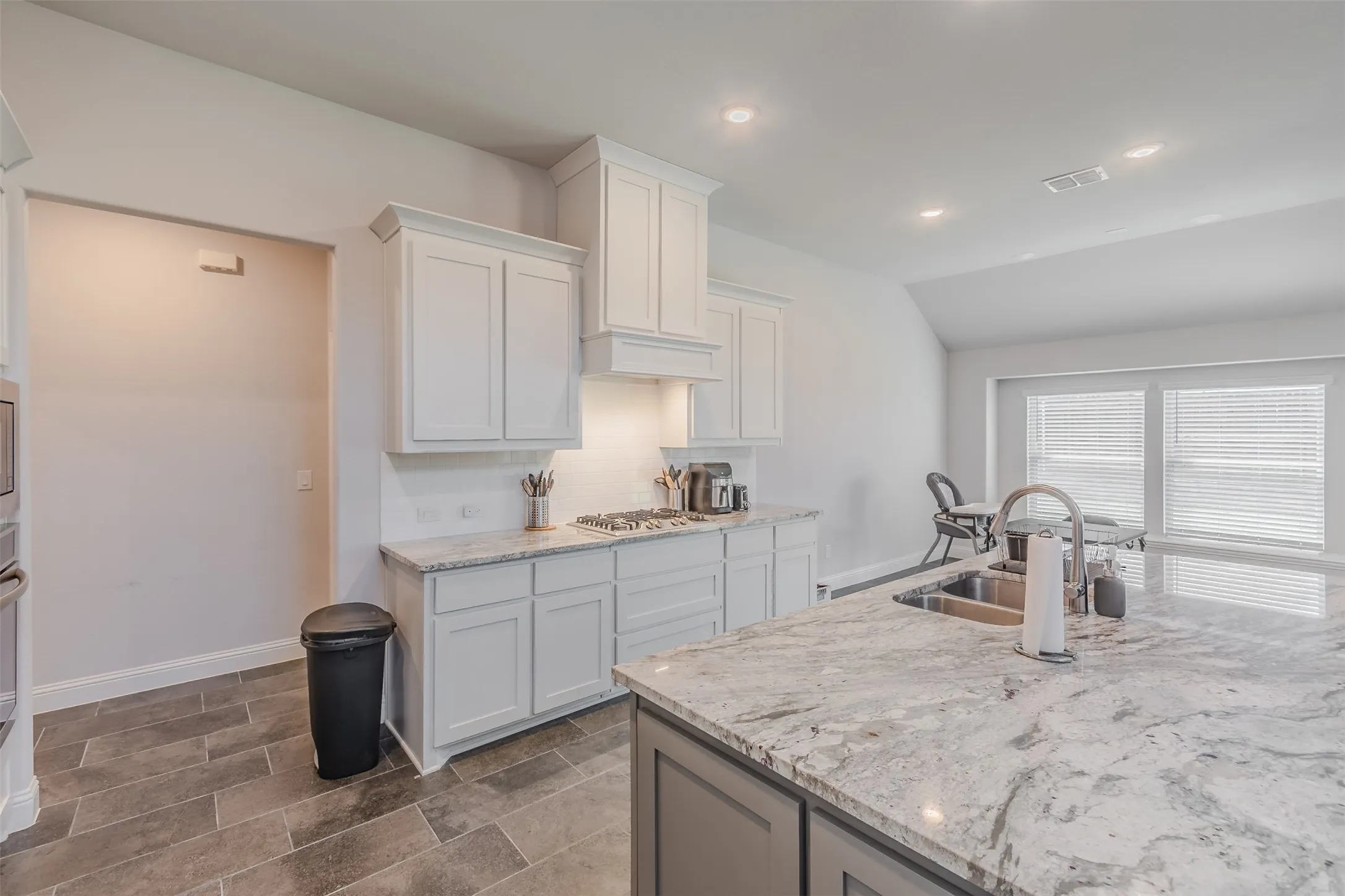 Kitchen featuring white cabinetry, light stone countertops, lofted ceiling, recessed lighting, and stainless steel gas cooktop