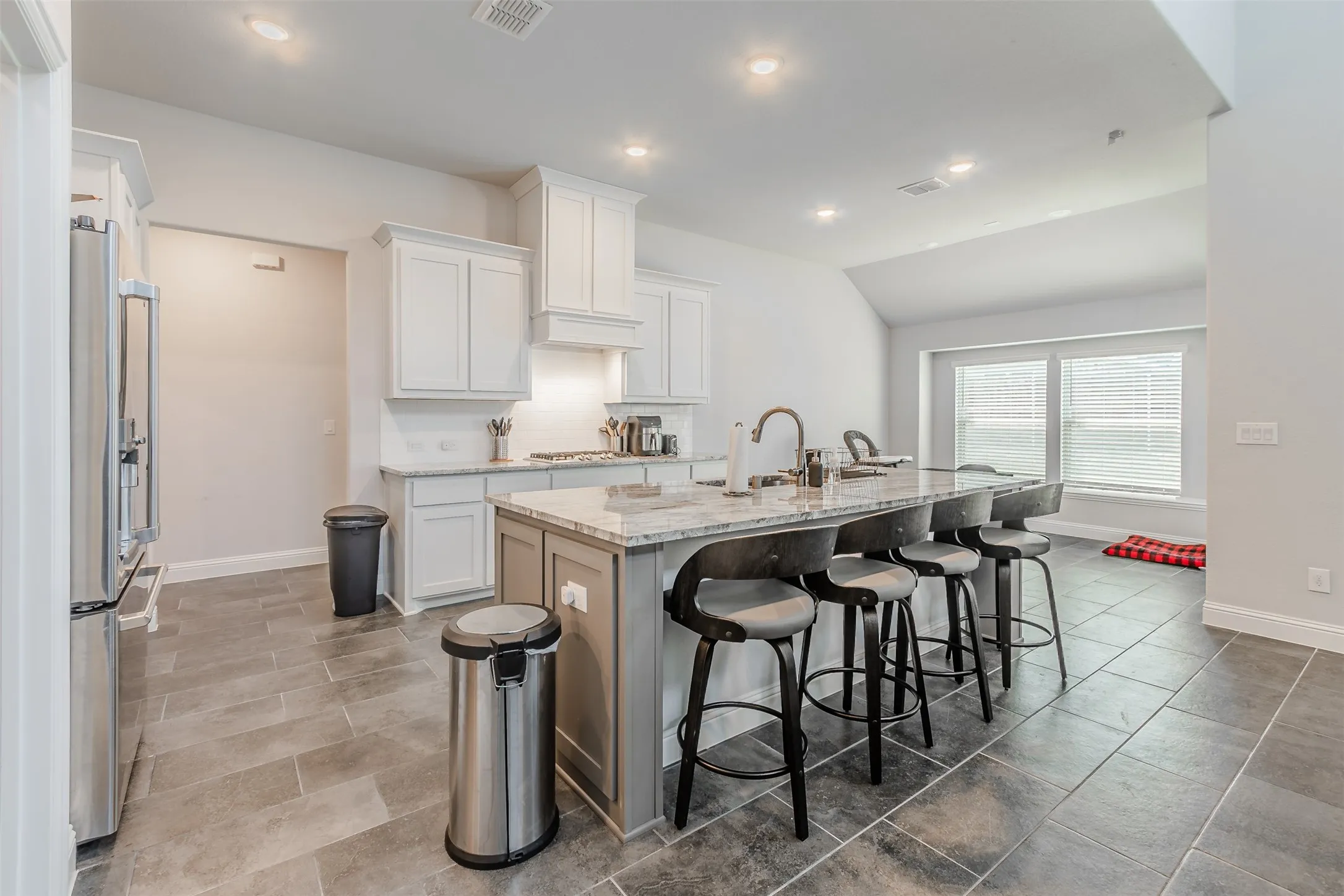 Kitchen with a kitchen breakfast bar, light stone counters, high quality fridge, a kitchen island with sink, and white cabinets