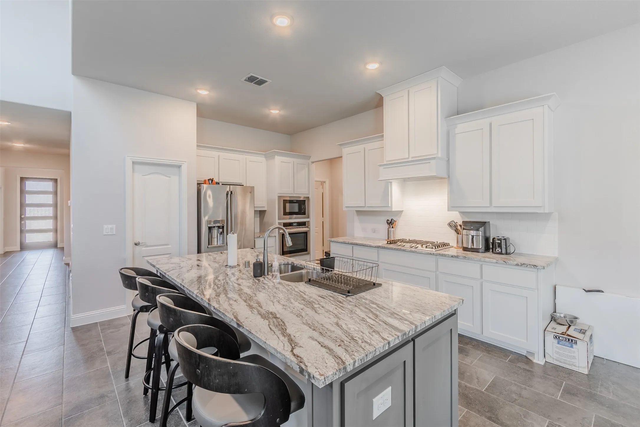Kitchen featuring a kitchen bar, stainless steel appliances, white cabinetry, light stone countertops, and an island with sink