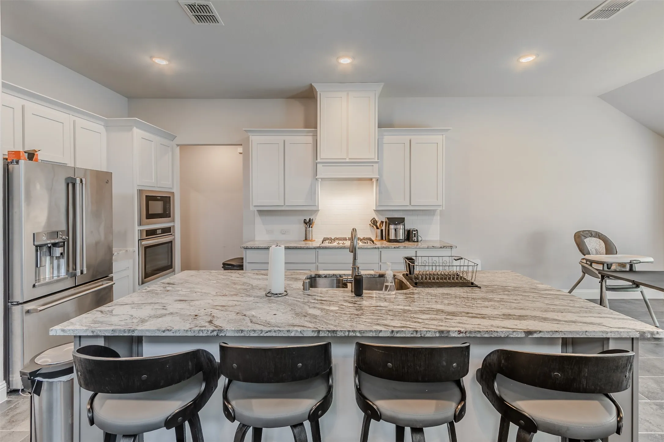 Kitchen featuring stainless steel appliances, a breakfast bar, a kitchen island with sink, white cabinetry, and light stone counters