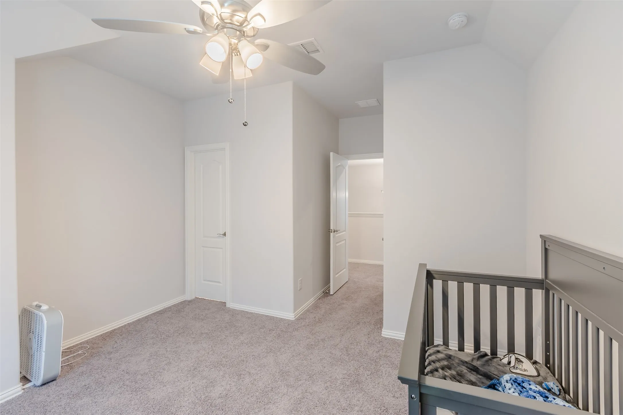 Bedroom featuring a nursery area, light carpet, and a ceiling fan