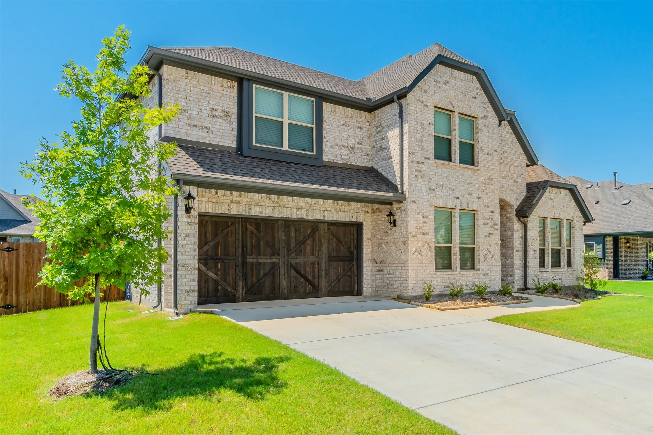 French country inspired facade featuring a garage, concrete driveway, brick siding, and a shingled roof
