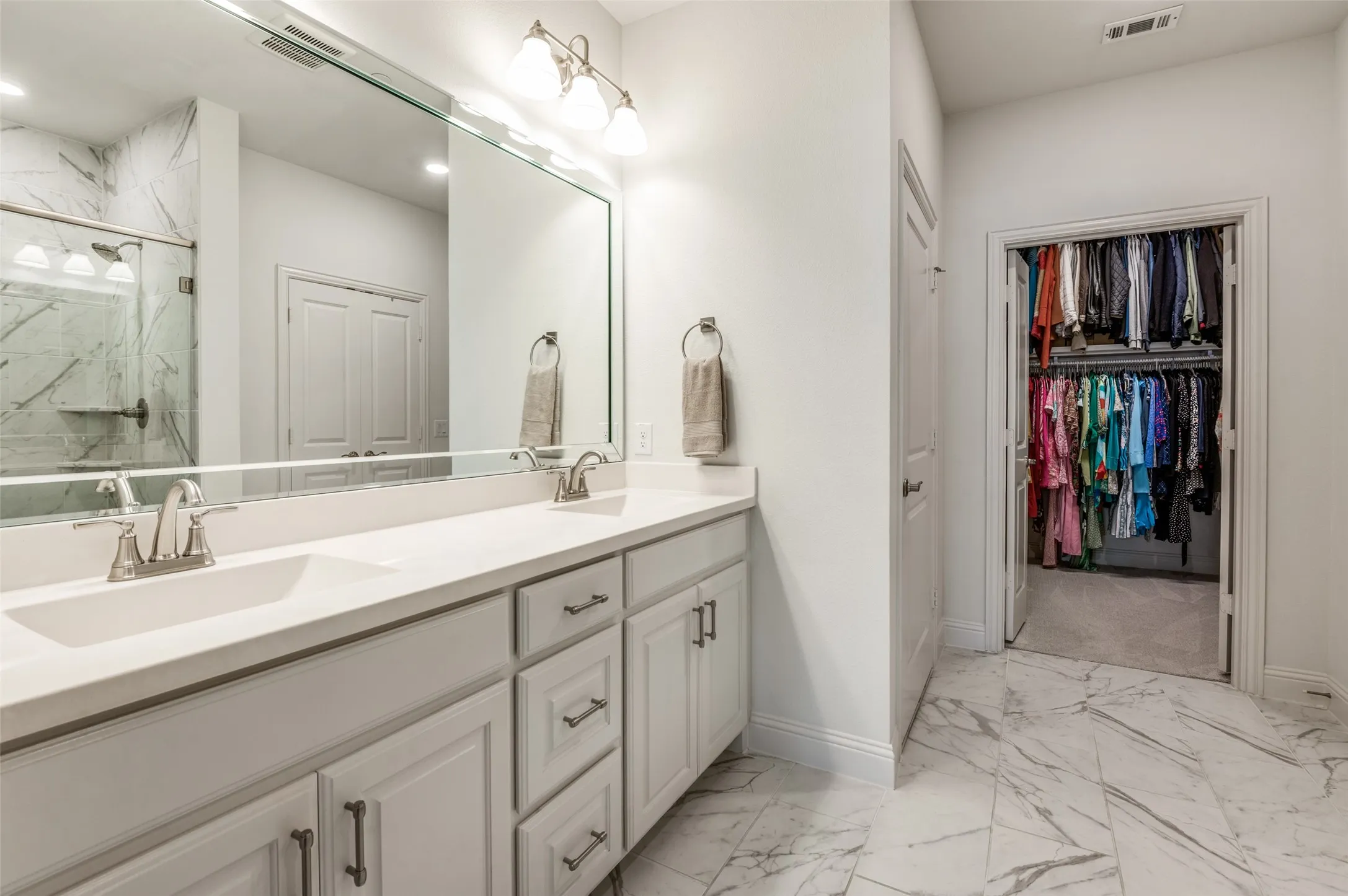 Expansive primary bathroom with dual sinks, marble-look tile flooring, and convenient access to the spacious walk-in closet.